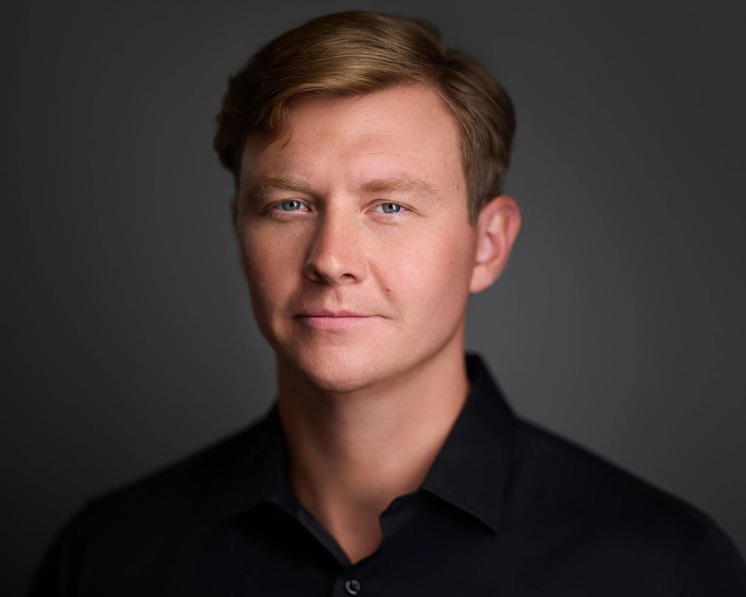 Scottsdale Headshot of a young man with blue eyes, short light brown hair, and fair skin, wearing a black shirt against a dark gray background. copyright Tony Taafe