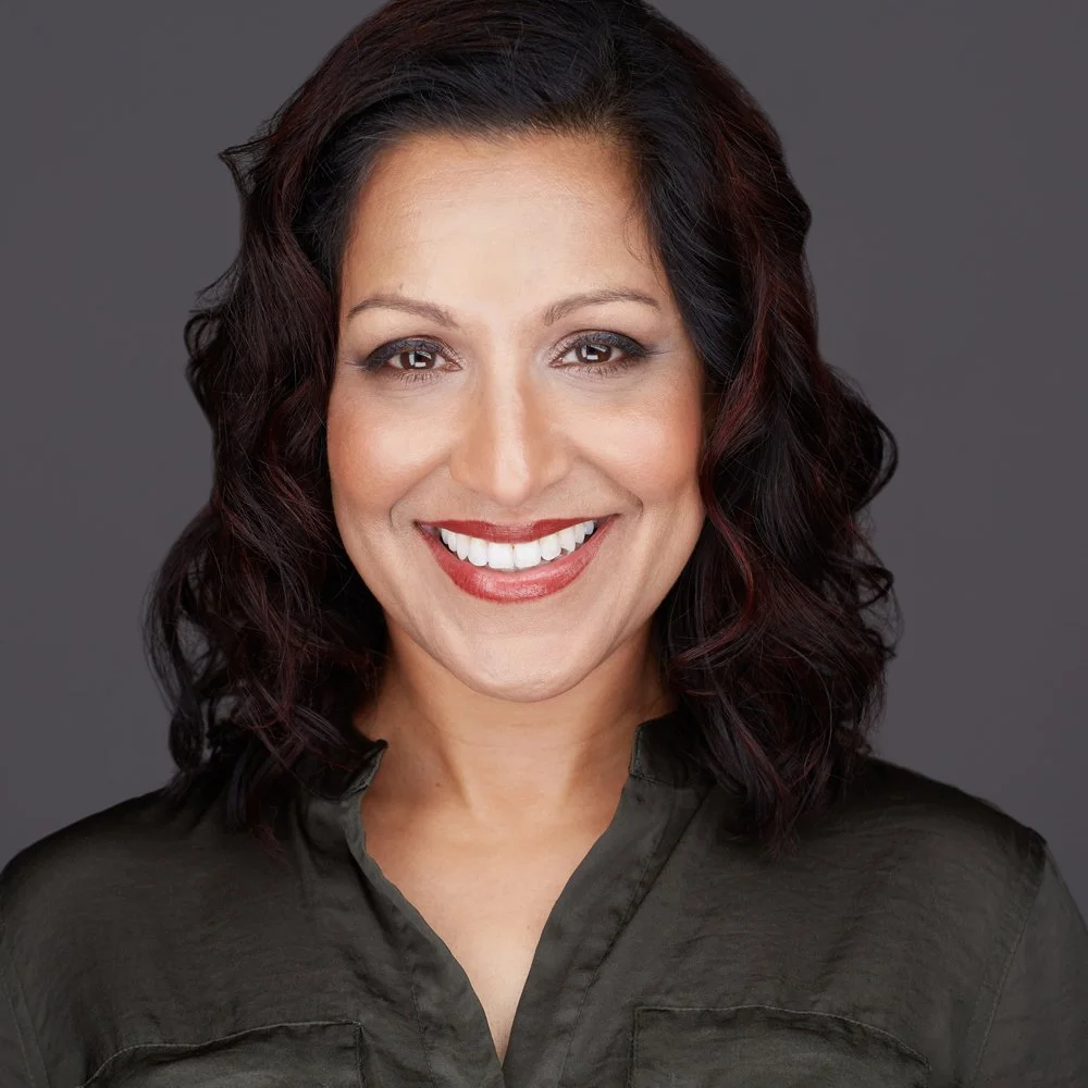 Headshot taken by Tony Taafe in Phoenix of a woman with shoulder-length dark wavy hair, smiling, wearing a dark gray shirt, against a gray background.