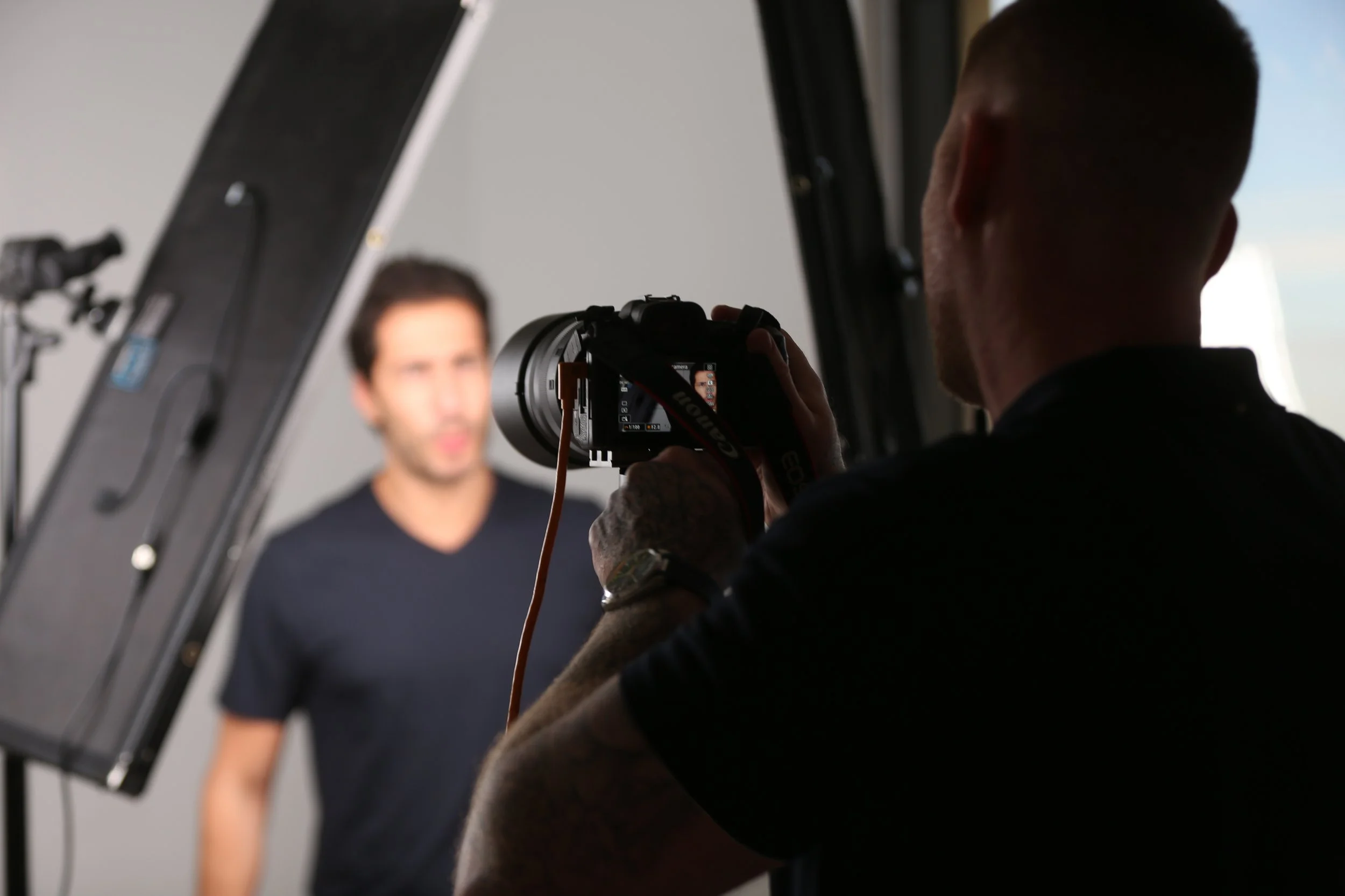 Photographer taking a Headshot portrait of a man in a studio with a gray background and photographic equipment visible.