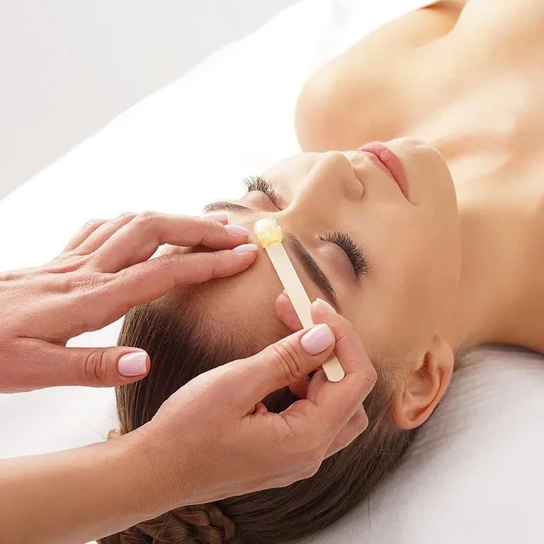 Person receiving eyebrow waxing treatment in spa setting.