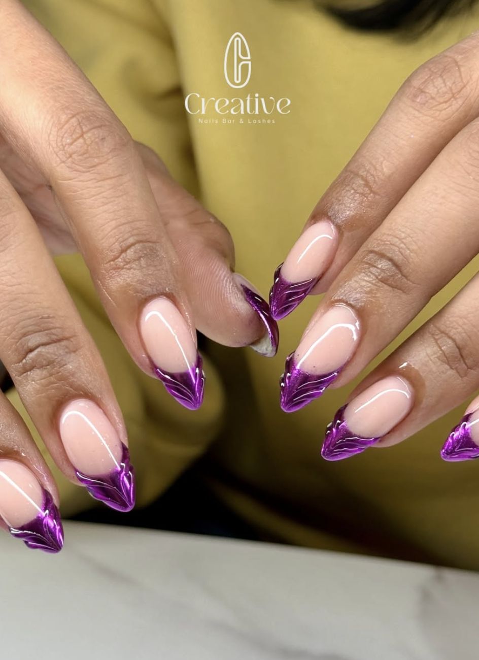 Close-up of hands with long, almond-shaped nails featuring a natural pink base and purple metallic French tips, with a logo for 'Creative Nails Bar & Lashes' in the background.