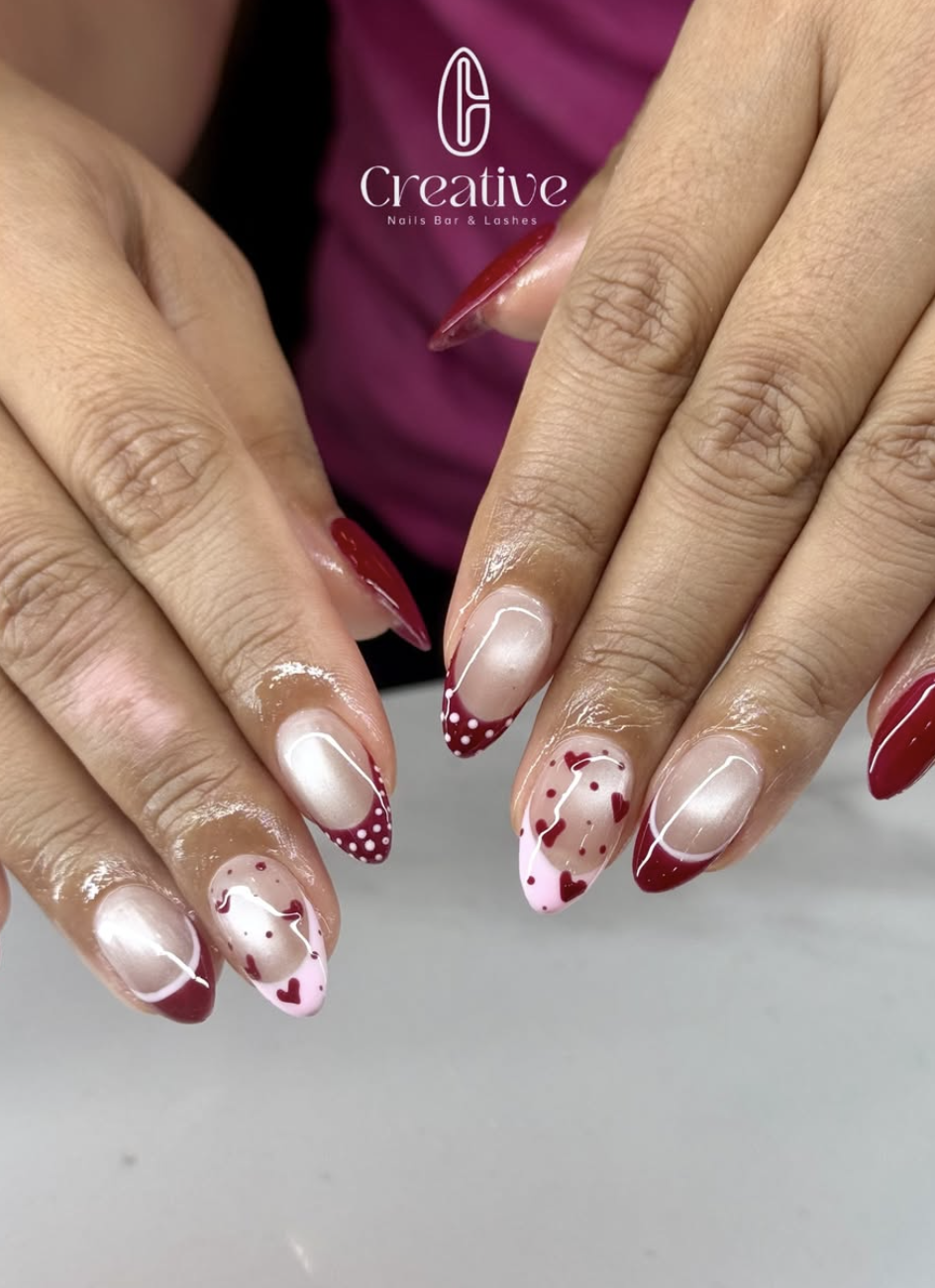 Manicured nails with red and white Valentine-themed designs, including hearts and dotted patterns.