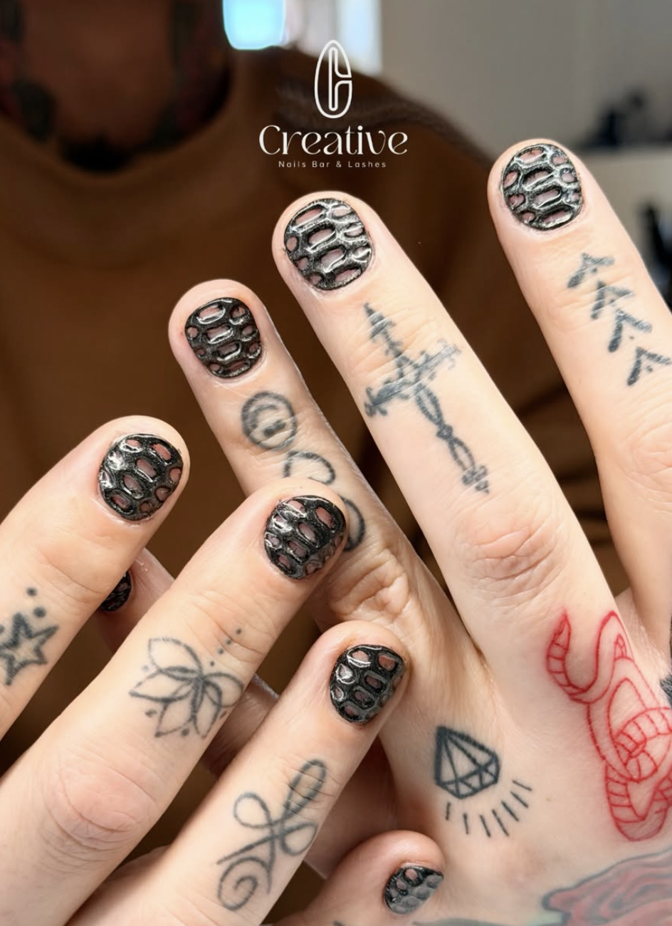 Close-up of hands with black, textured nail polish and various tattoos, including a dragon, a diamond, and arrows.