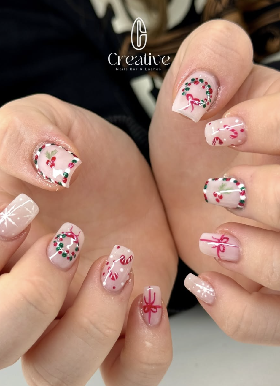 Festive holiday nail art with white base, decorated with red and green Christmas-themed designs including holly, wreaths, candy canes, and red ribbons.