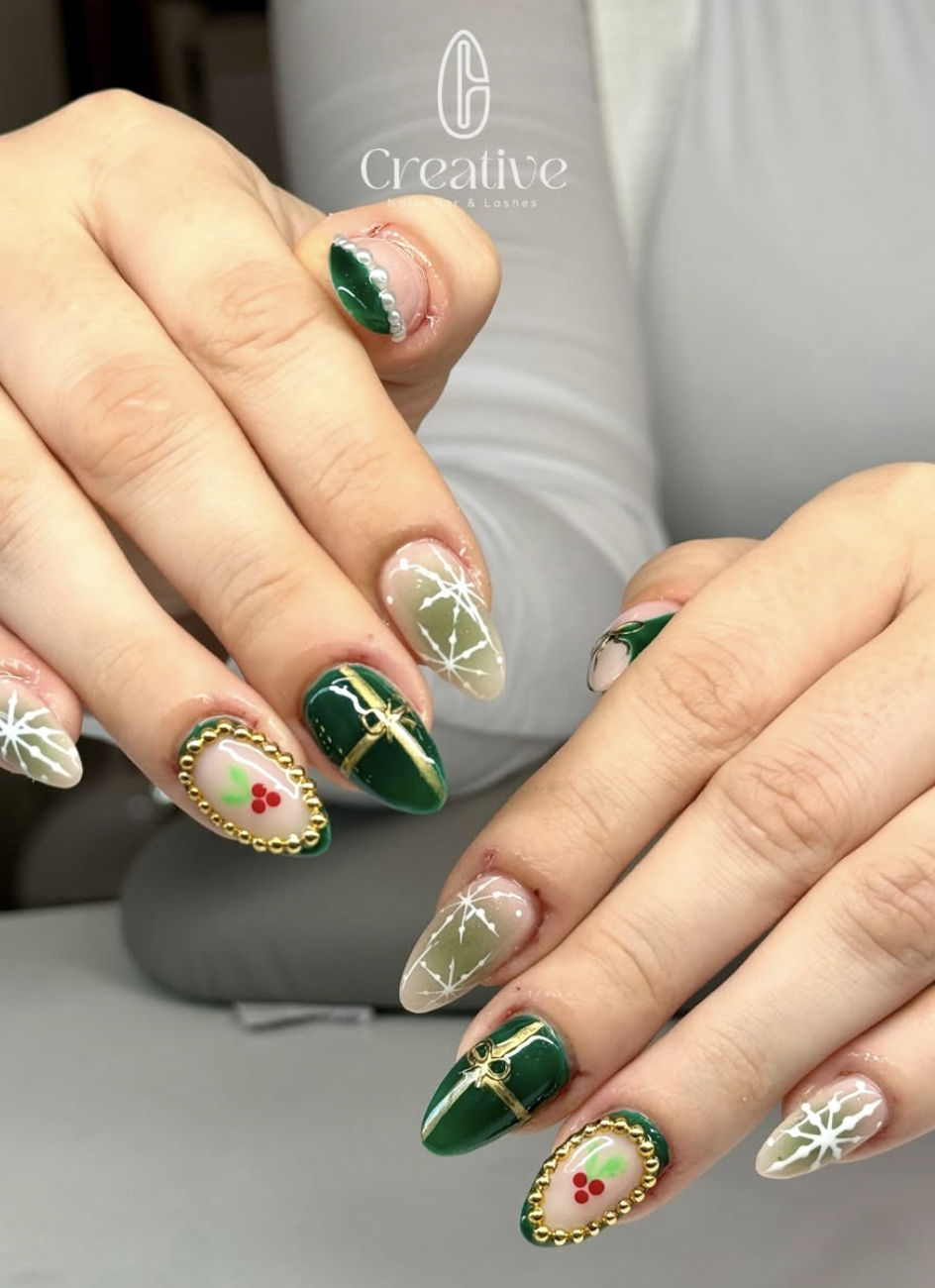 Christmas-themed nail art with green, white, and gold colors, decorated with snowflakes, holly berries, and gold chain outlines.