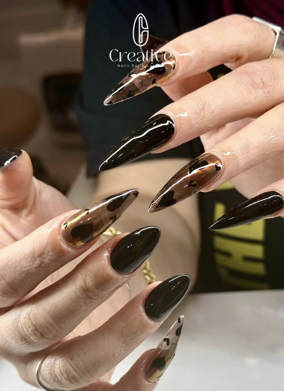 Close-up of a woman's hands showing long, pointed acrylic nails with a black and gold tortoiseshell design.