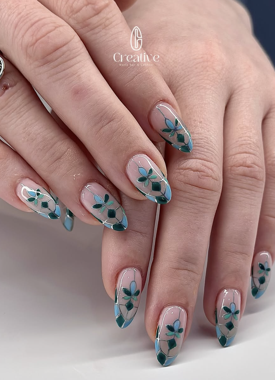 Close-up of hands with manicured nails featuring blue and green floral nail art on a clear base.