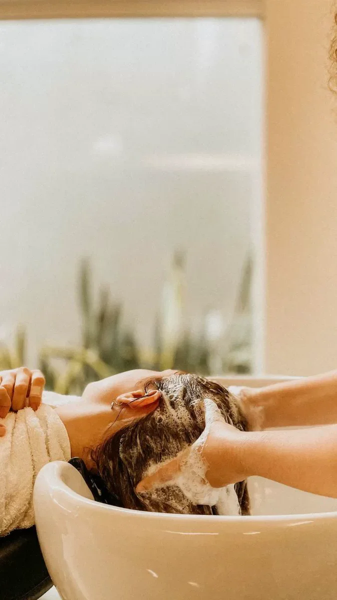 Person getting a hair wash at a salon, with hair covered in shampoo and their head resting in a sink basin.