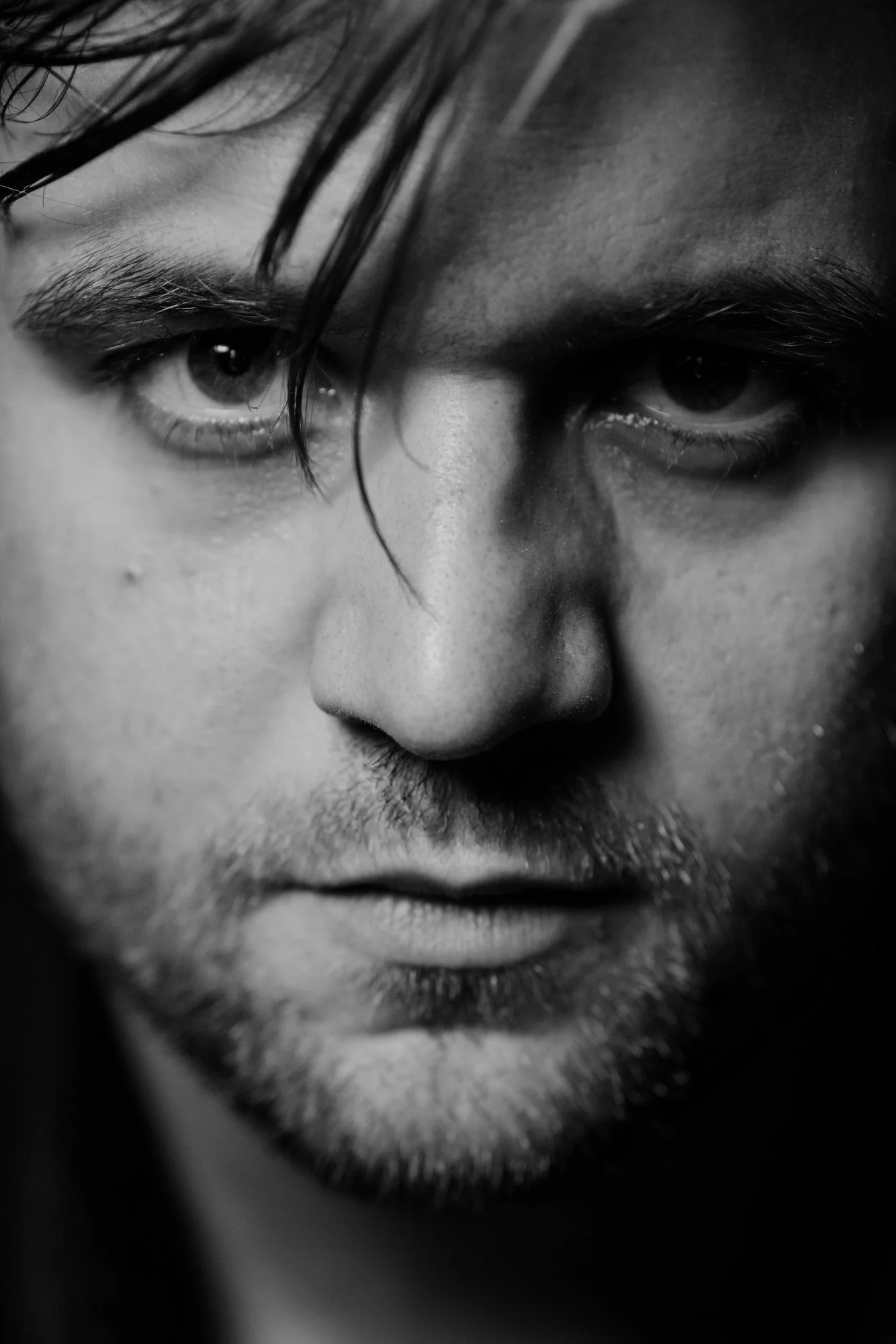 Close-up black and white photo of a person's intense gaze, focusing on one eye with slightly wet eyelashes, showing a serious expression.