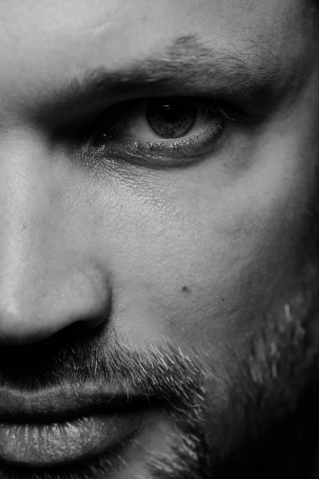 Close-up black and white photograph of a person's eye, including eyebrow, eyelashes, and surrounding skin.