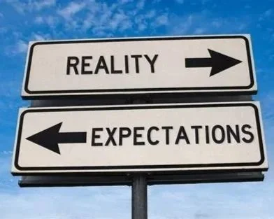 A road sign with two directions: 'Reality' pointing to the right and 'Expectations' pointing to the left.