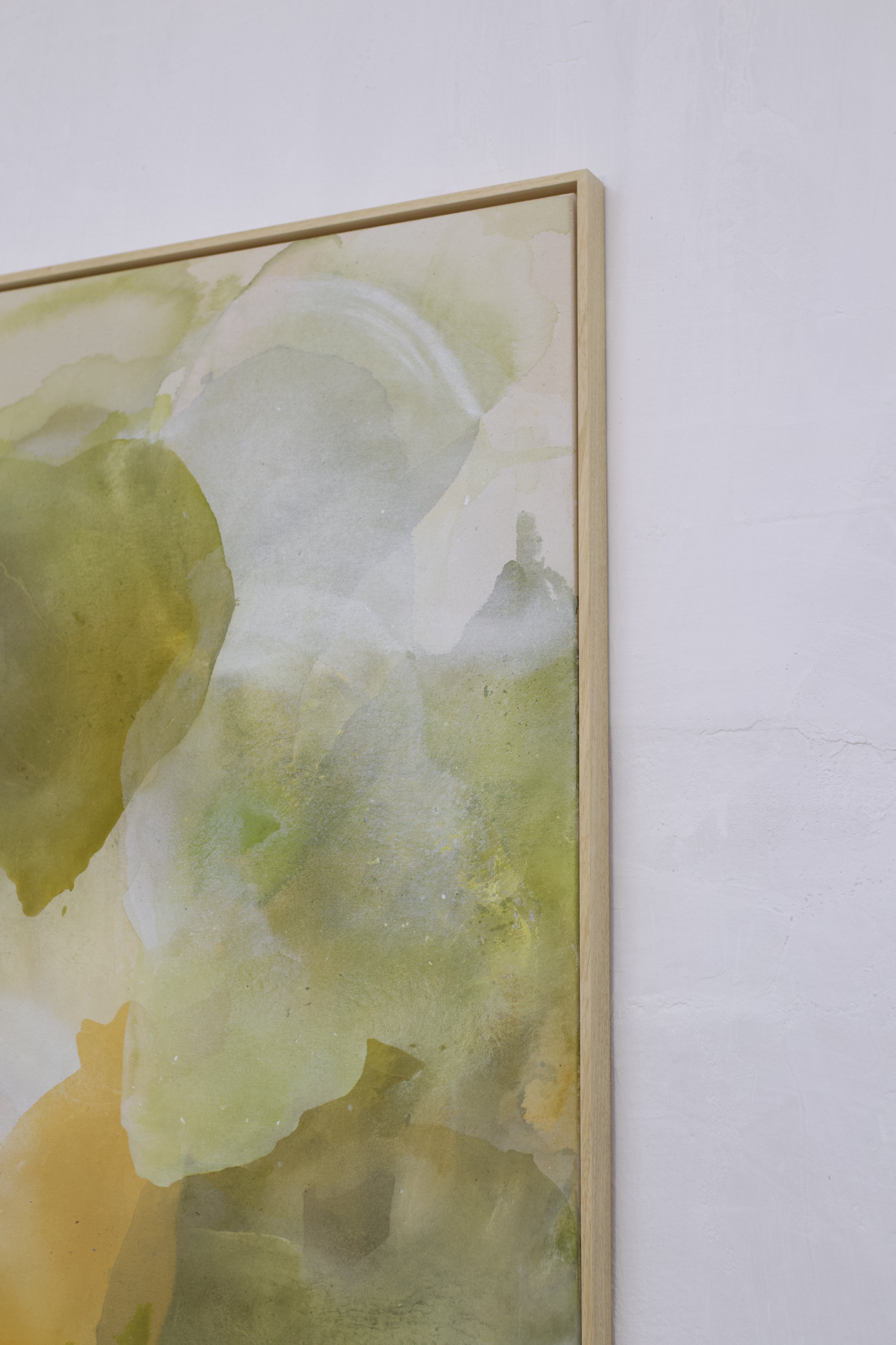 Ein Kunstwerk mit grünen und gelben Wasserfarben, rahmenlos, an einer weißen Wand.
