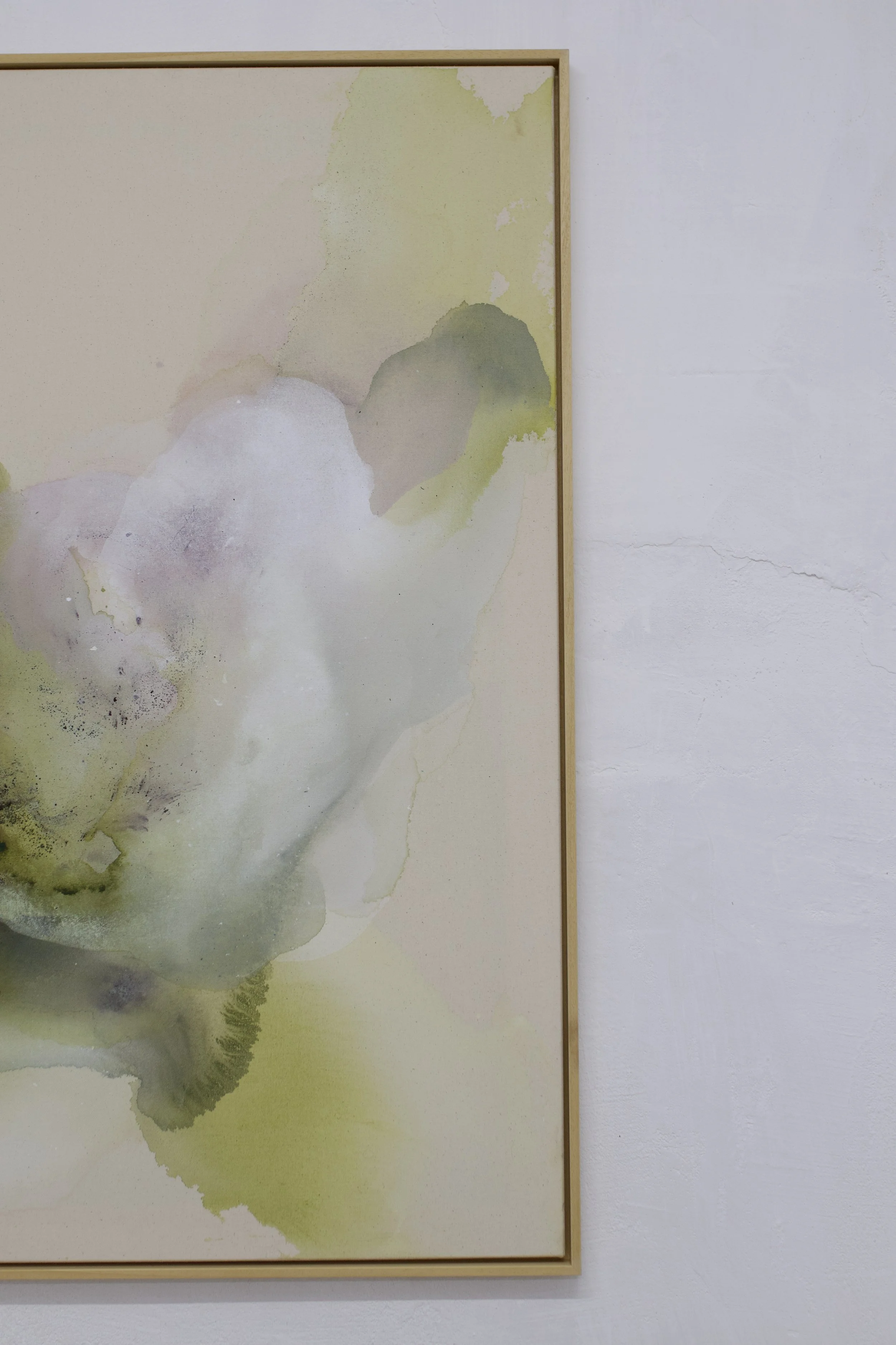 Aquarellbild mit hellen grünen, gelben, lilafarbenen und grauen Farbtönen, in einem einfachen Holzrahmen an einer weißen Wand