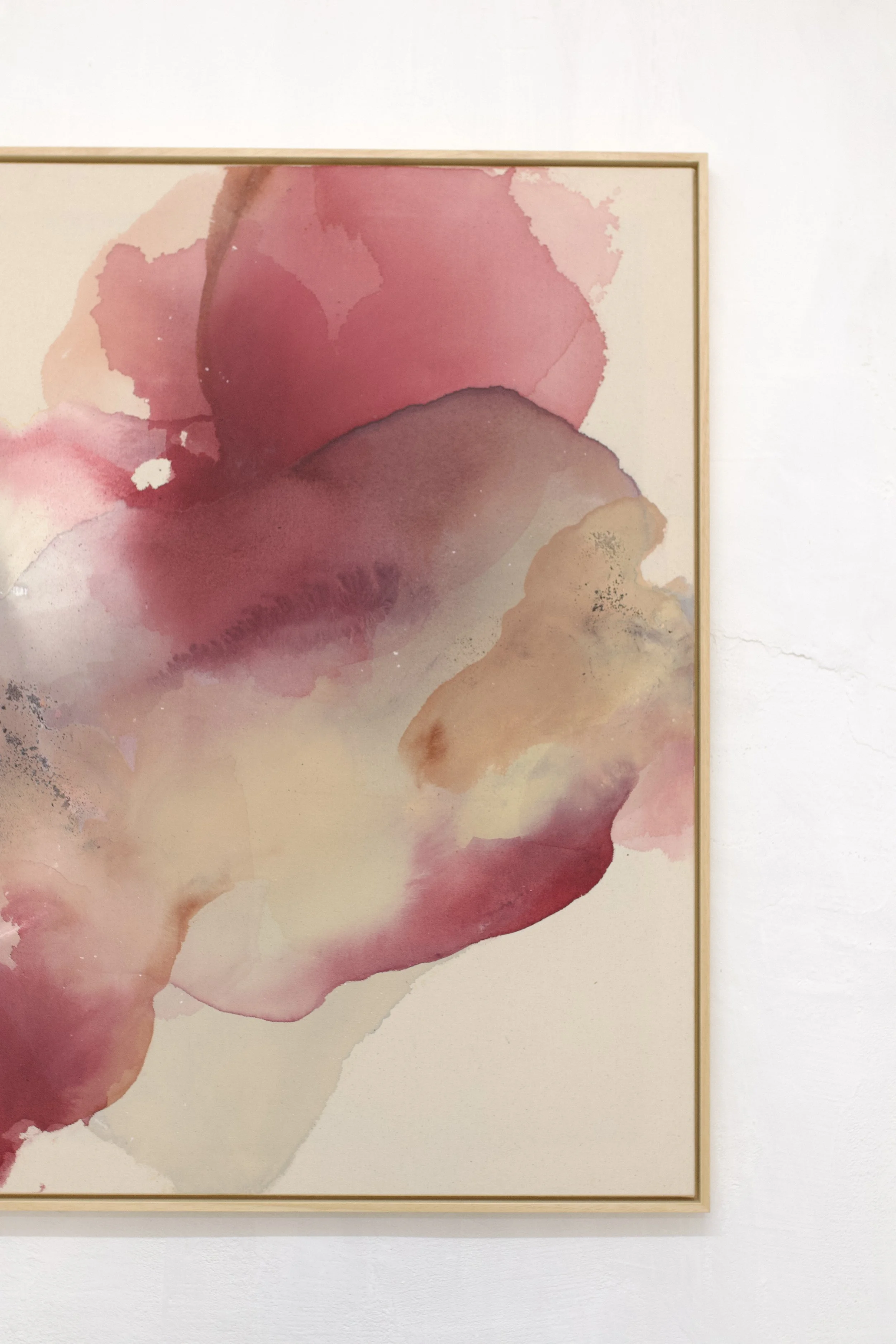 Ein abstraktes Gemälde mit pinken, lila und beige Wasserfarben auf Leinwand, gerahmt und an einer weißen Wand befestigt.