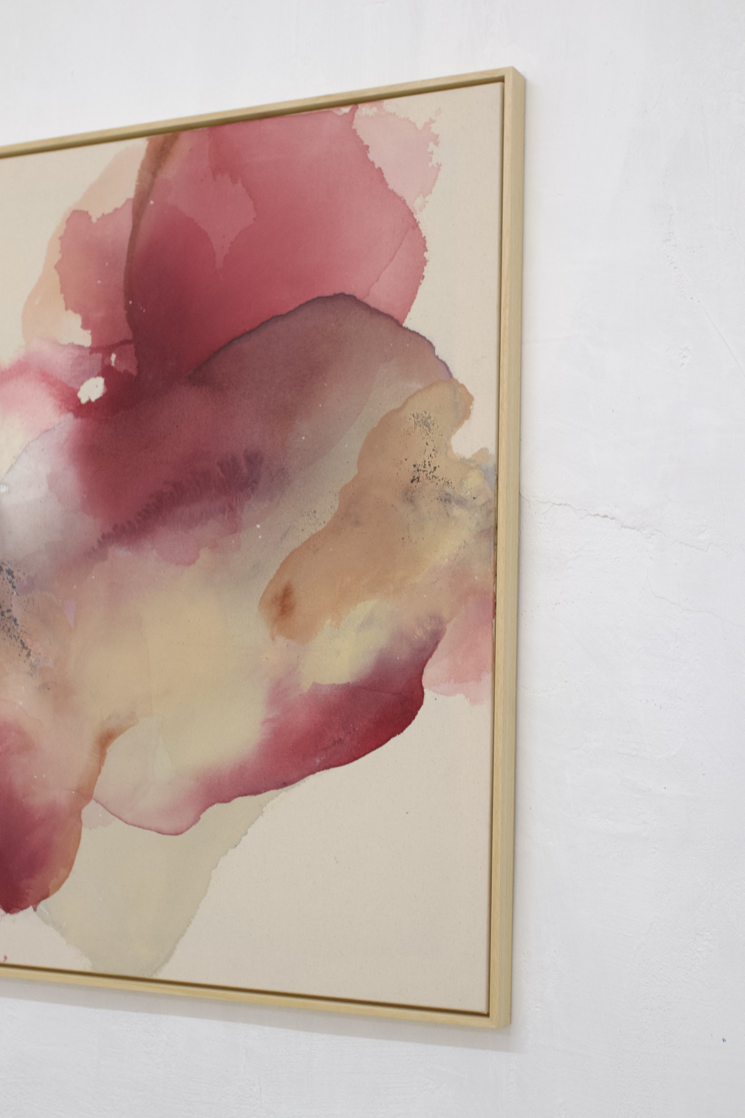 Aquarellkunstwerk mit pinken und beigen Farbtönen in einem Holzrahmen an einer weißen Wand.