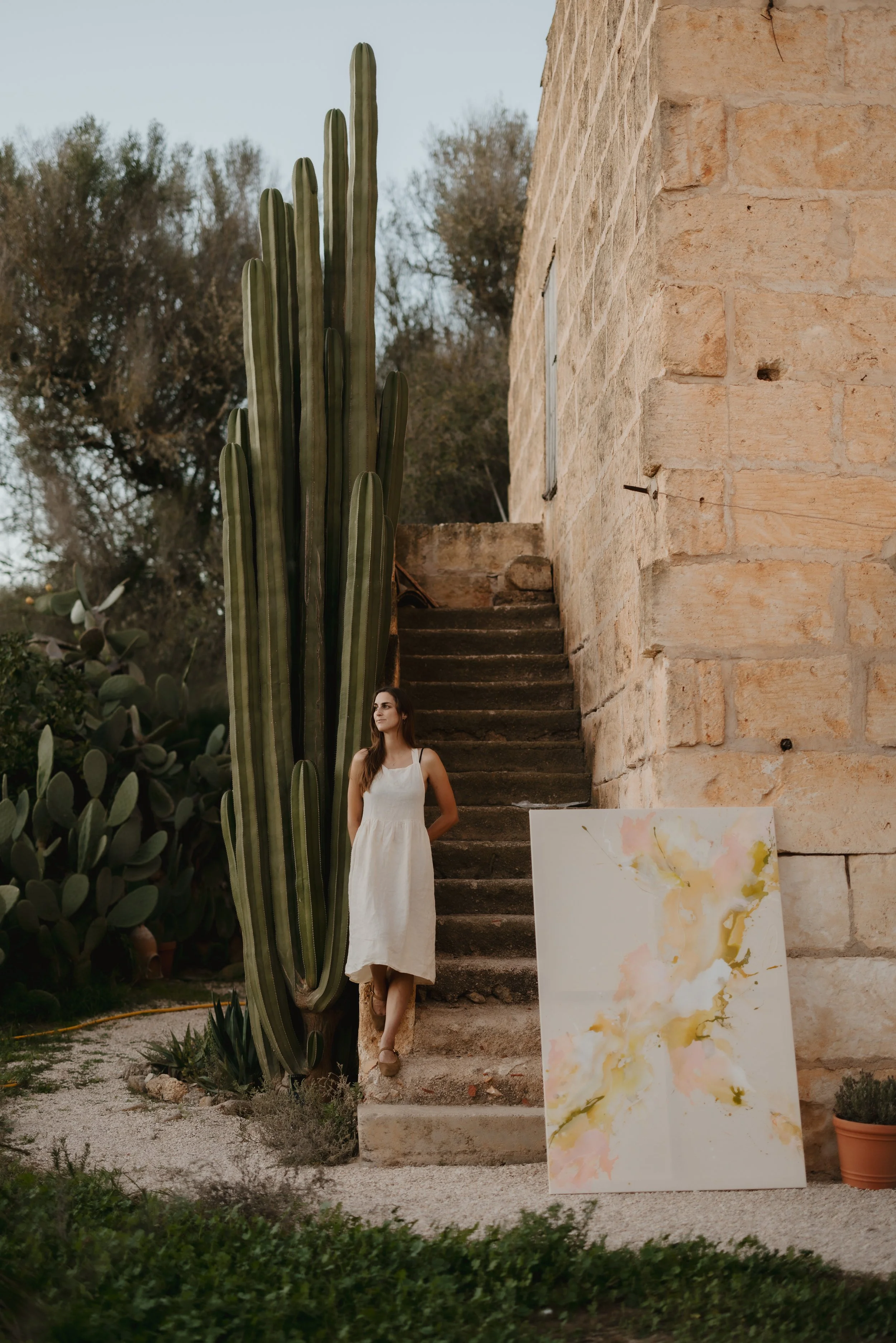 Contemporary artist Denize Jung presenting her abstract artwork in front of her Mediterranean finca in Mallorca, surrounded by nature and a large cactus.