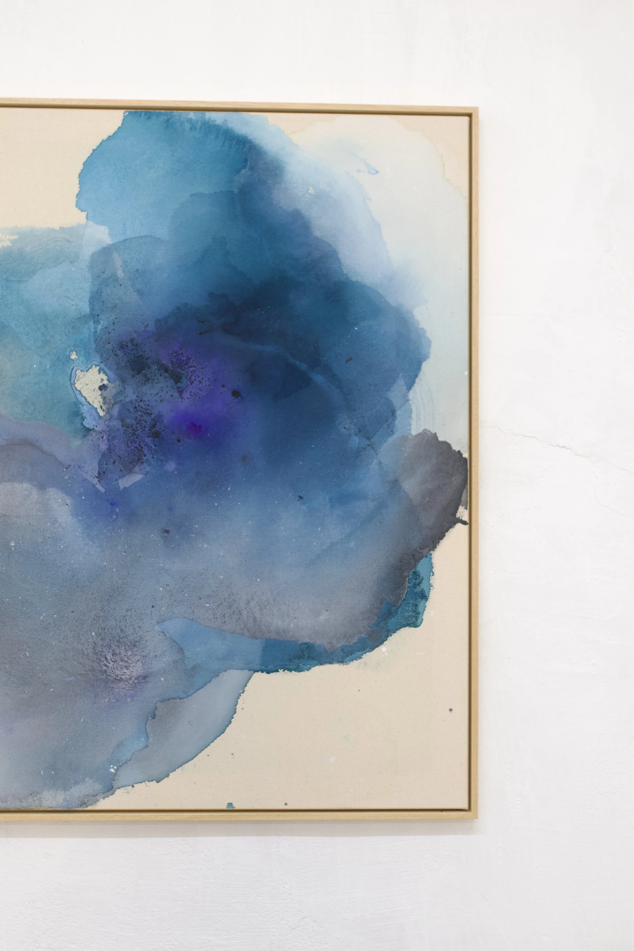 Aquarellgemälde mit verschiedenen Blautönen in einem Holzrahmen an einer weißen Wand.