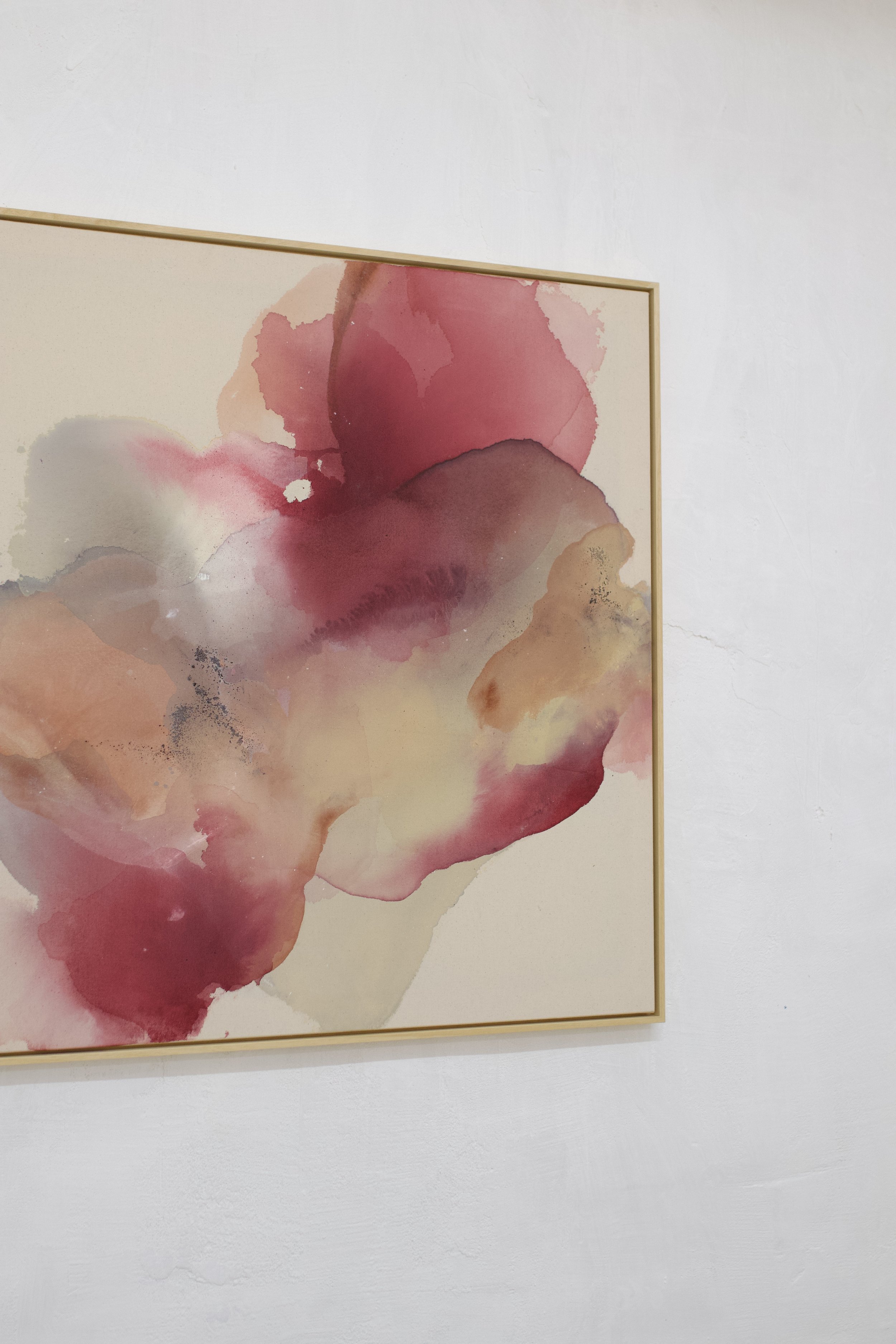 Abstraktes Gemälde mit rosa und beigen Wasserfarben auf Leinwand, eingerahmt, an weißer Wand. 
