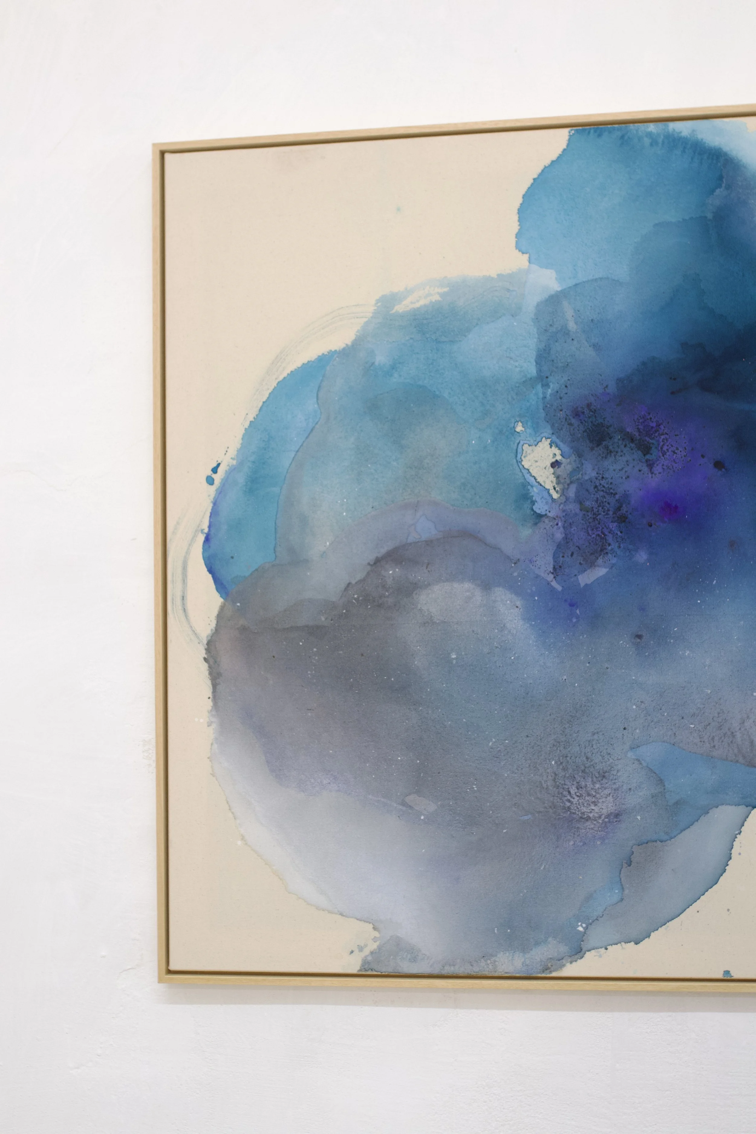 Ein abstraktes Gemälde in Blau-, Grau- und Weißtönen, das mit Aquarelltechniken erstellt wurde, hängt an einer weißen Wand.