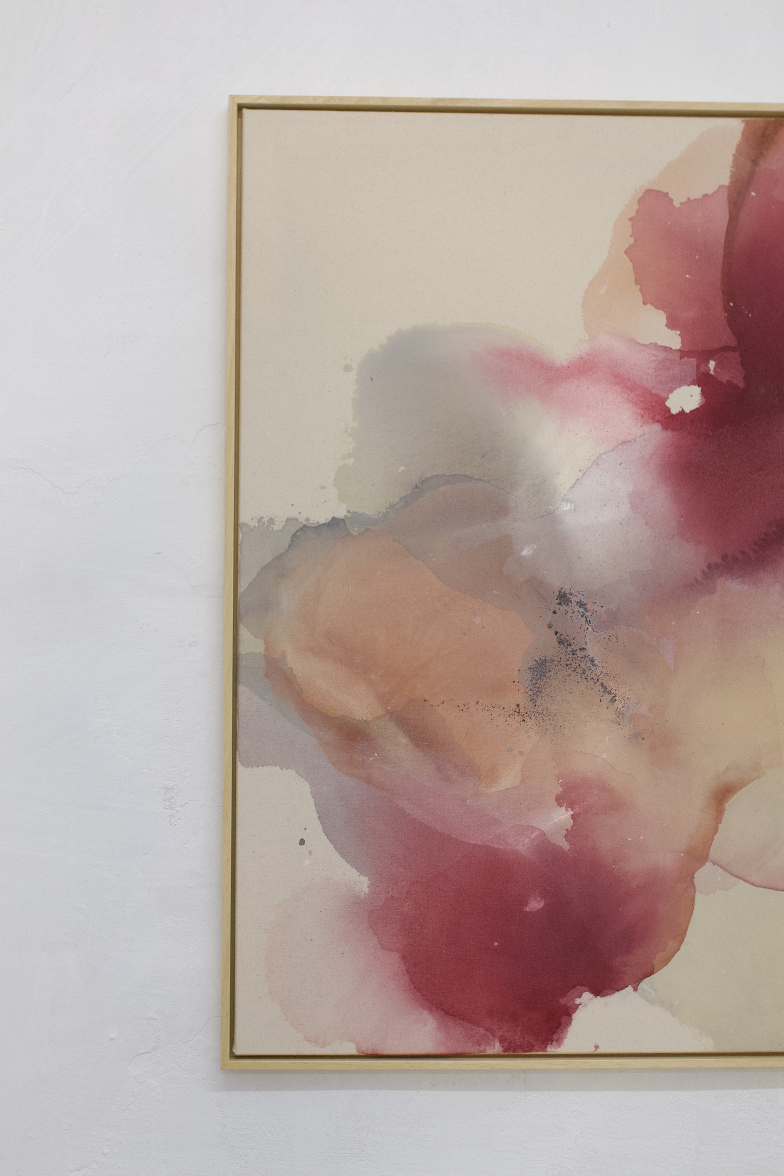 Abstraktes Wasserfarbenkunstwerk mit pinken, roten, grauen und braunen Tönen, eingerahmt in einen dünnen, leichten Rahmen, an einer weißen Wand aufgehängt.
