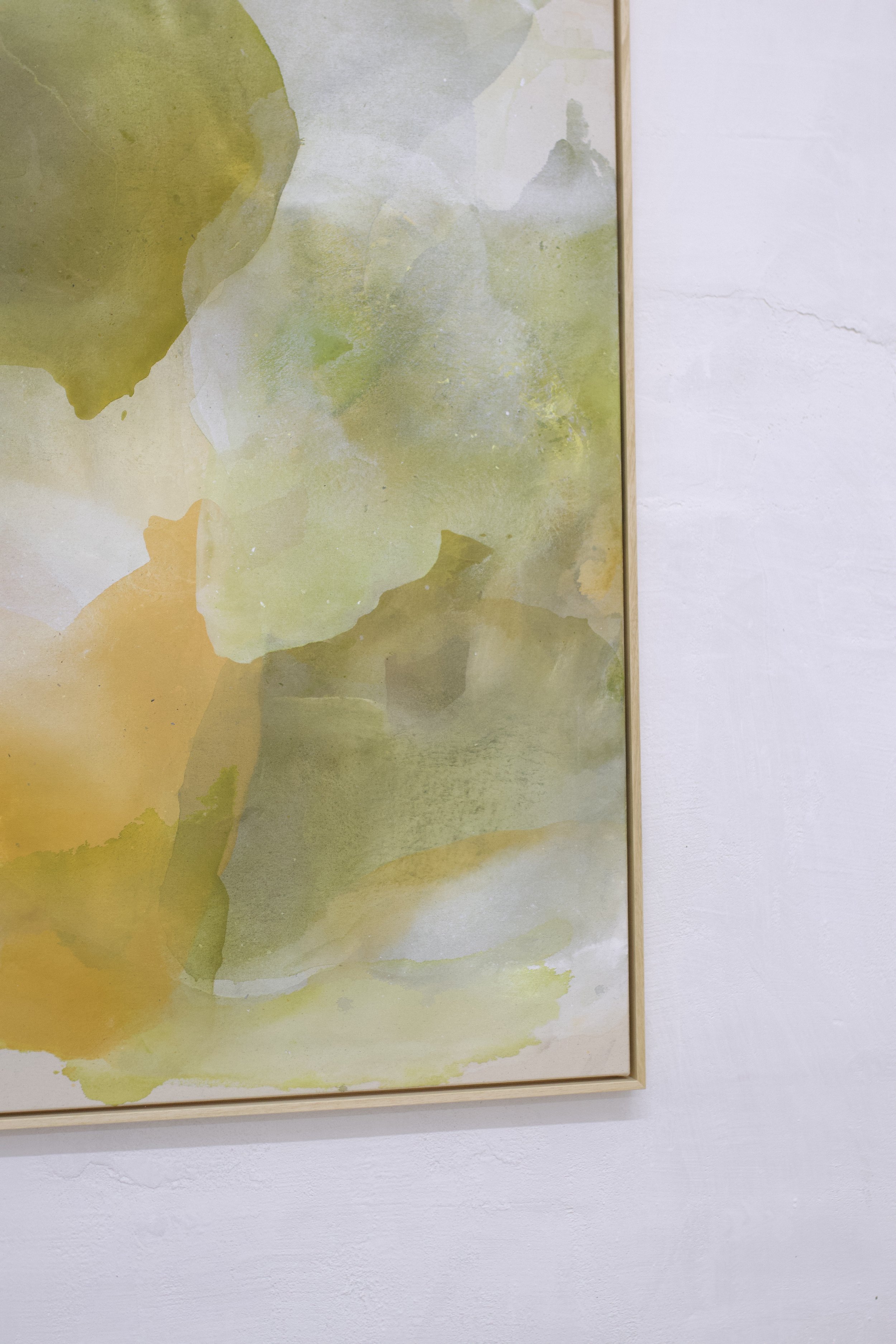 Abstrakte grüne und gelbe Aquarellmalerei auf Leinwand, gerahmt, an einer weißen Wand aufgehängt.