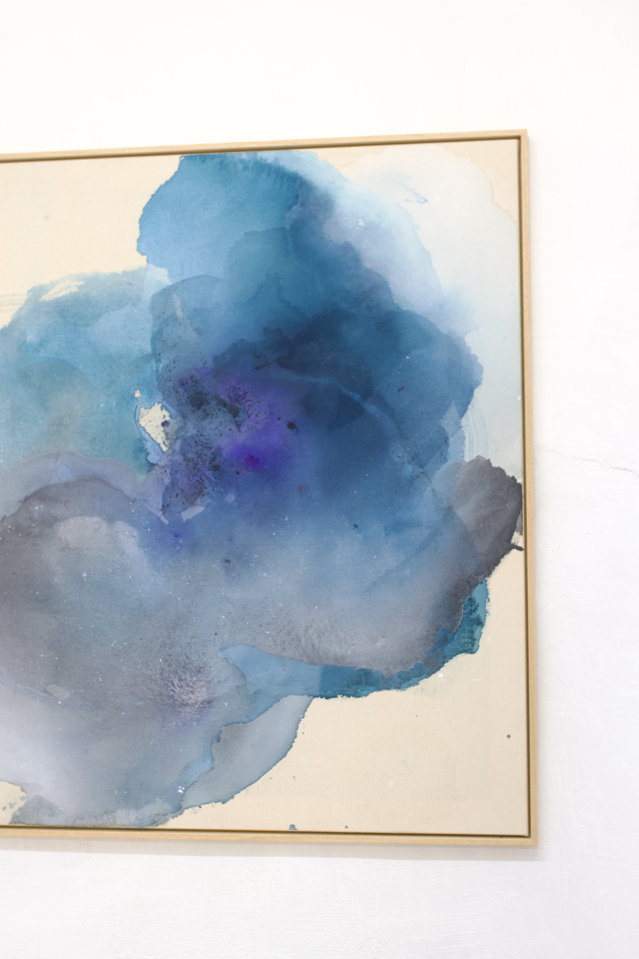 Aquarellbild in Blau- und Grautönen, gerahmt an einer weißen Wand.