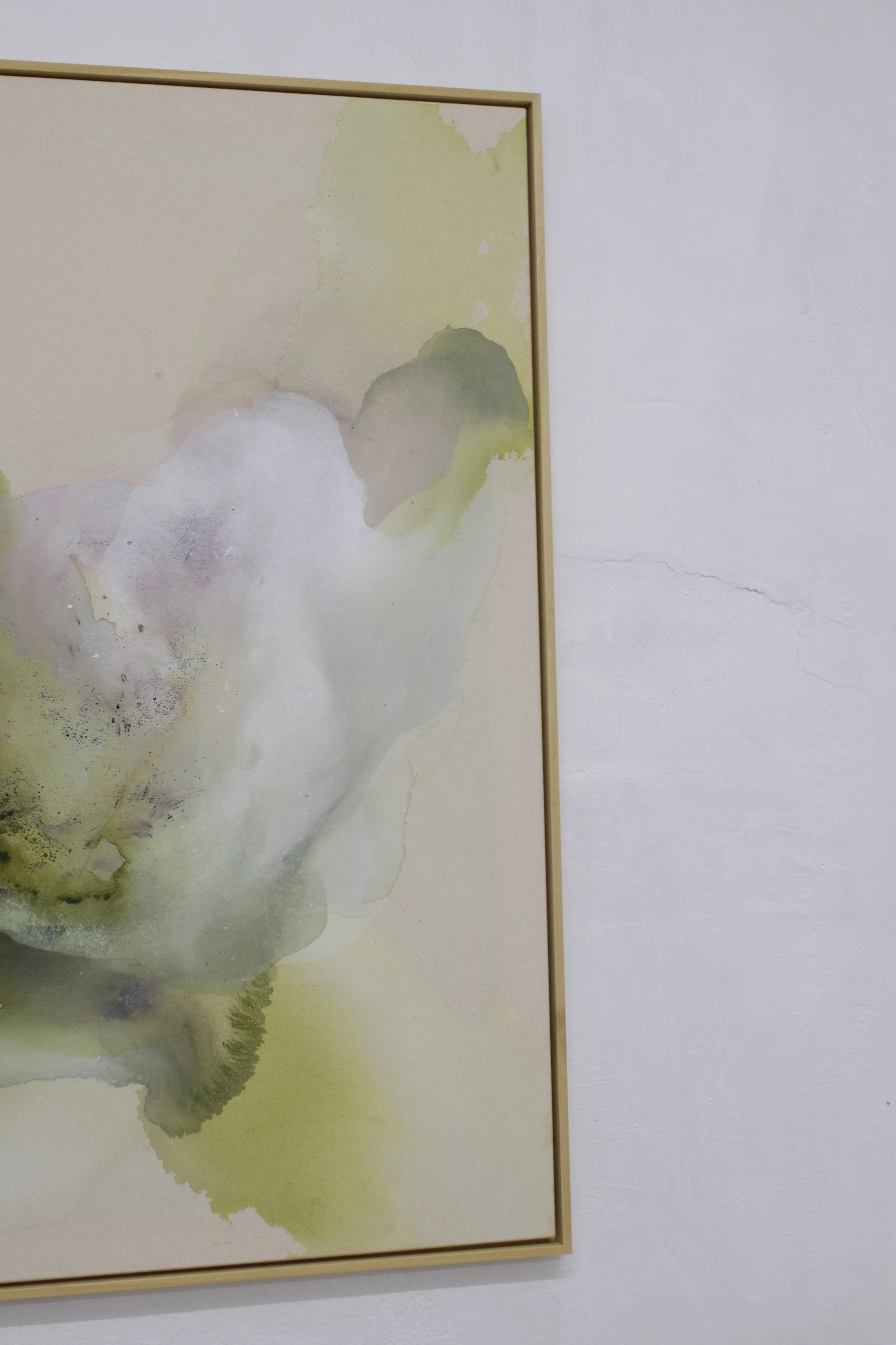 Aquarellartwork mit grünlichen und weißen Farbverläufen, umgeben von einem dünnen Holzrahmen, an einer weißen Wand.