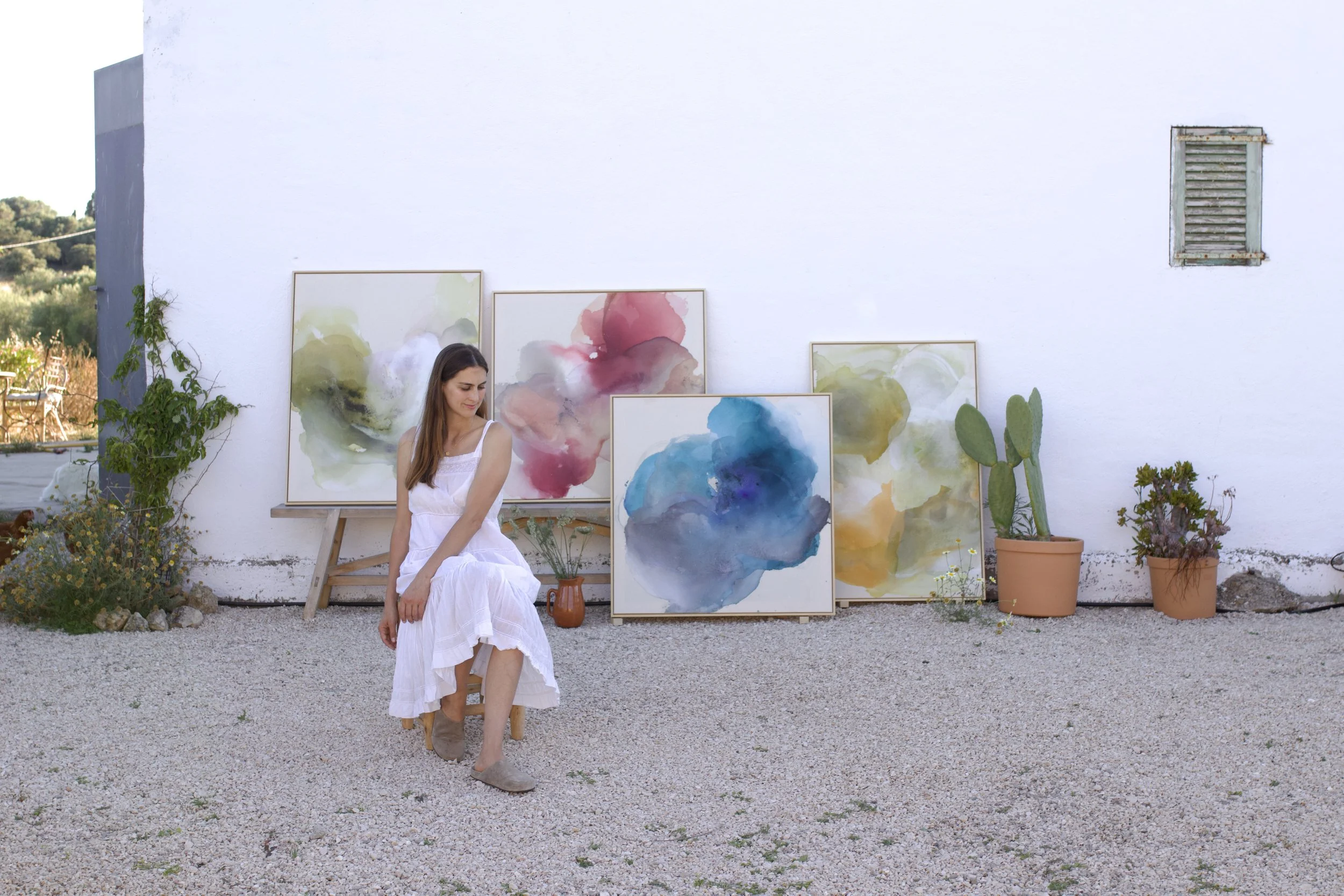Denize Jung showcasing a collection of original abstract artworks in her Mediterranean garden studio in Mallorca.