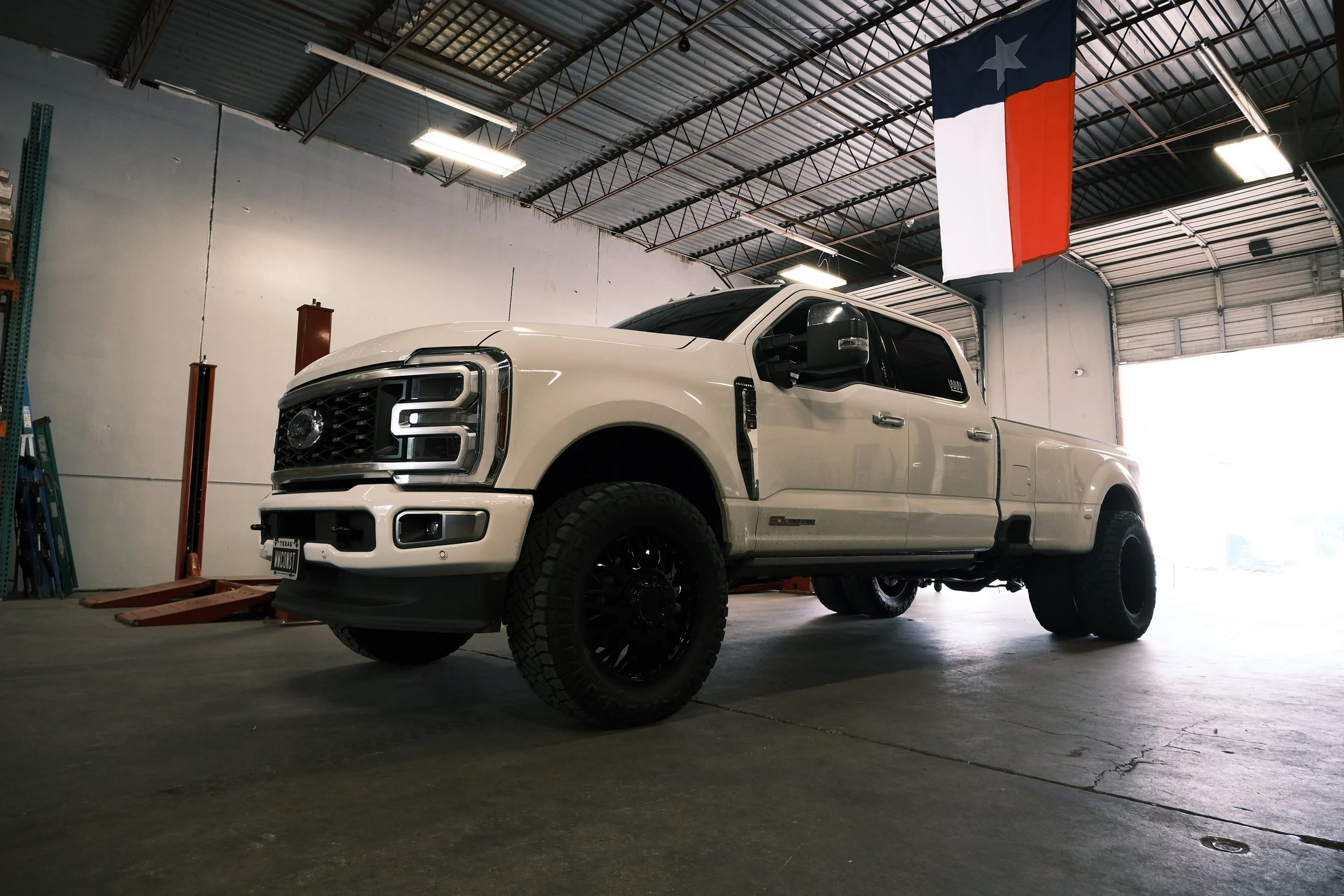 A white Ford pickup truck inside a garage with a Texas flag hanging from the ceiling.