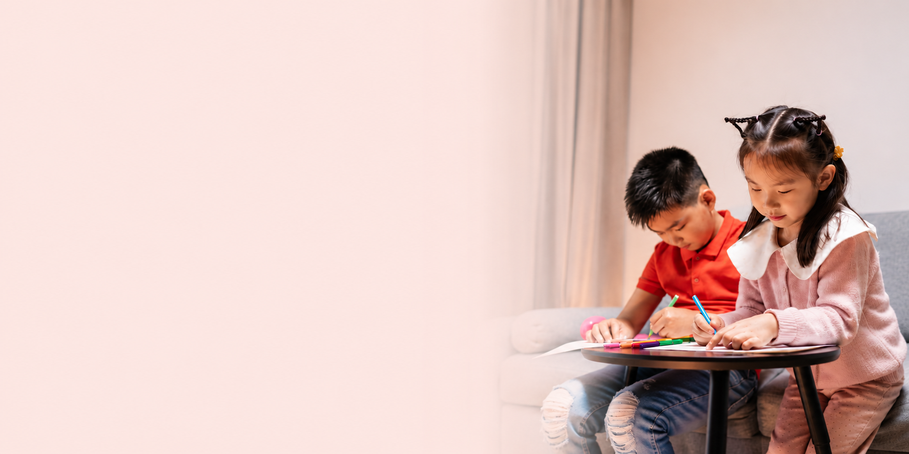 Two children sitting at a table drawing with colored markers in a cozy room.