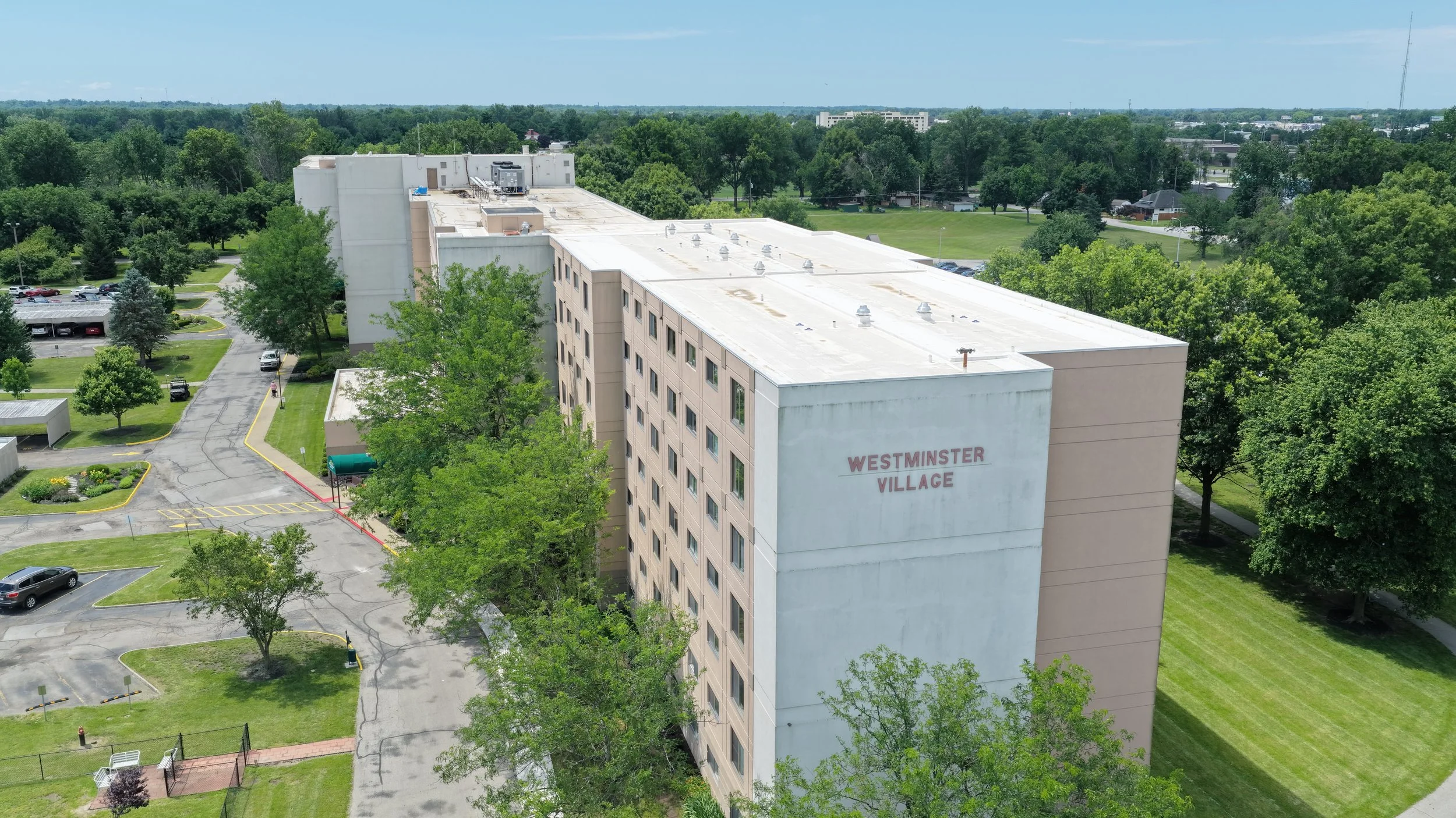 Aerial view of Westminster Village residential building surrounded by green trees and parking lot.