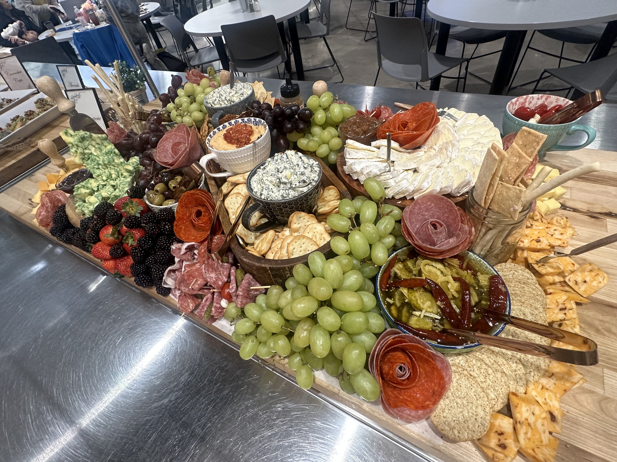 A large assortment of appetizers including grapes, assorted cheeses, crackers, sliced cured meats, dips, salsa, and vegetables on a buffet table at a gathering.