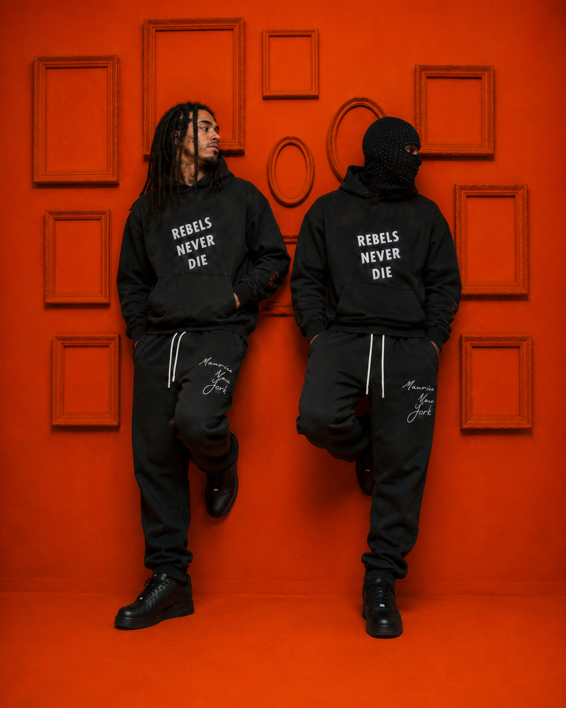 Two men in black hoodies and sweatpants pose against an orange wall with empty picture frames. Both are wearing black sneakers; one has a face mask. The hoodies say 'REBELS NEVER DIE.' The sweatpants have handwritten text 'Maurice New York'.