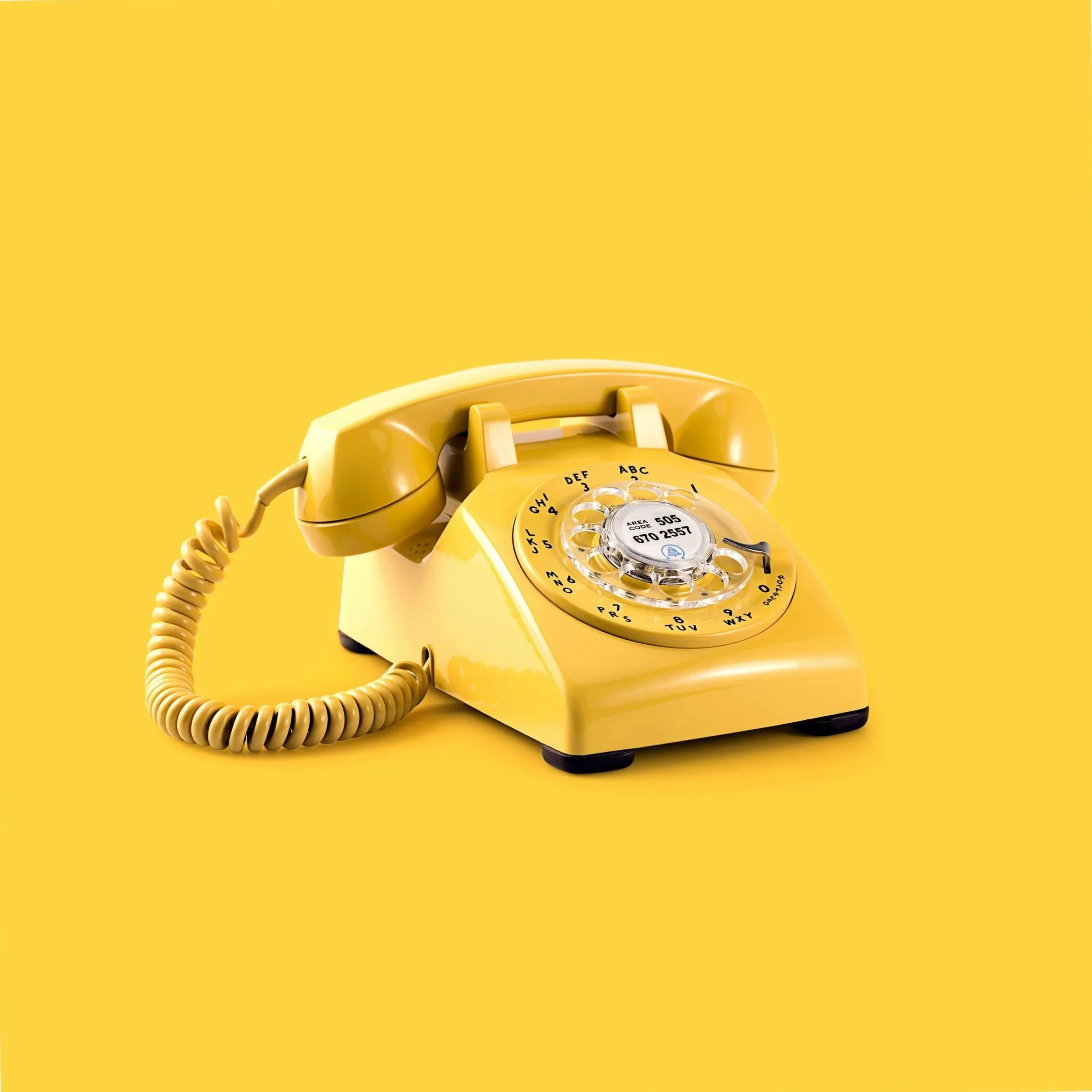 Close-up of a vintage yellow rotary telephone with a coiled cord against a yellow background.
