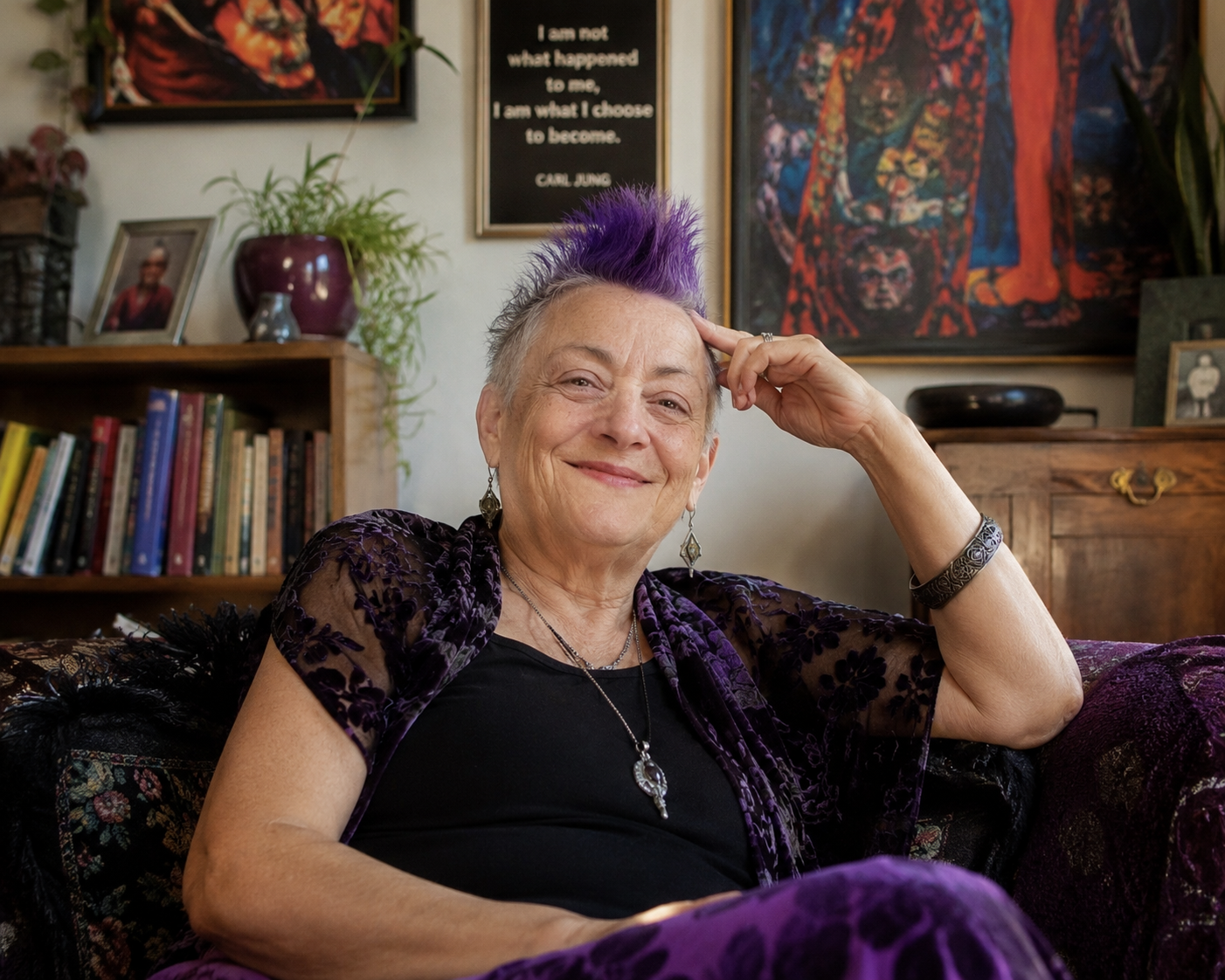 A smiling elderly woman with a purple mohawk hairstyle sitting on a purple velvet couch in a cozy room, surrounded by books, artwork, and framed photos.