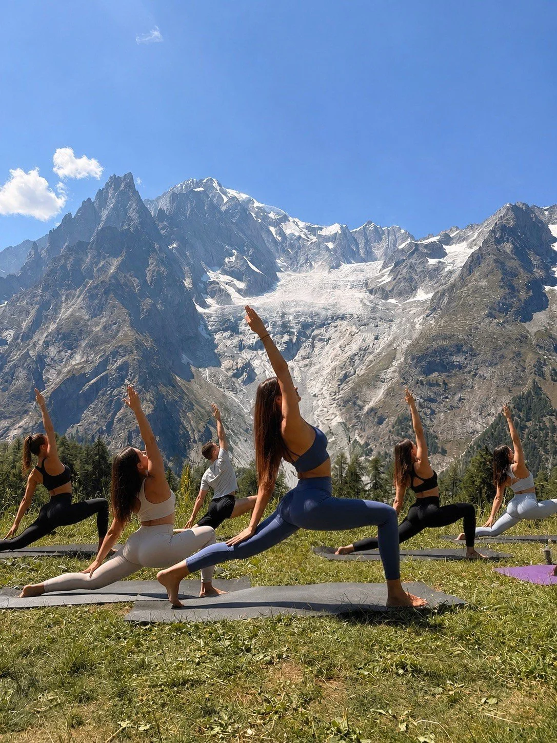 A group of people practicing yoga outdoors on mats with a mountain range and glacier in the background.
