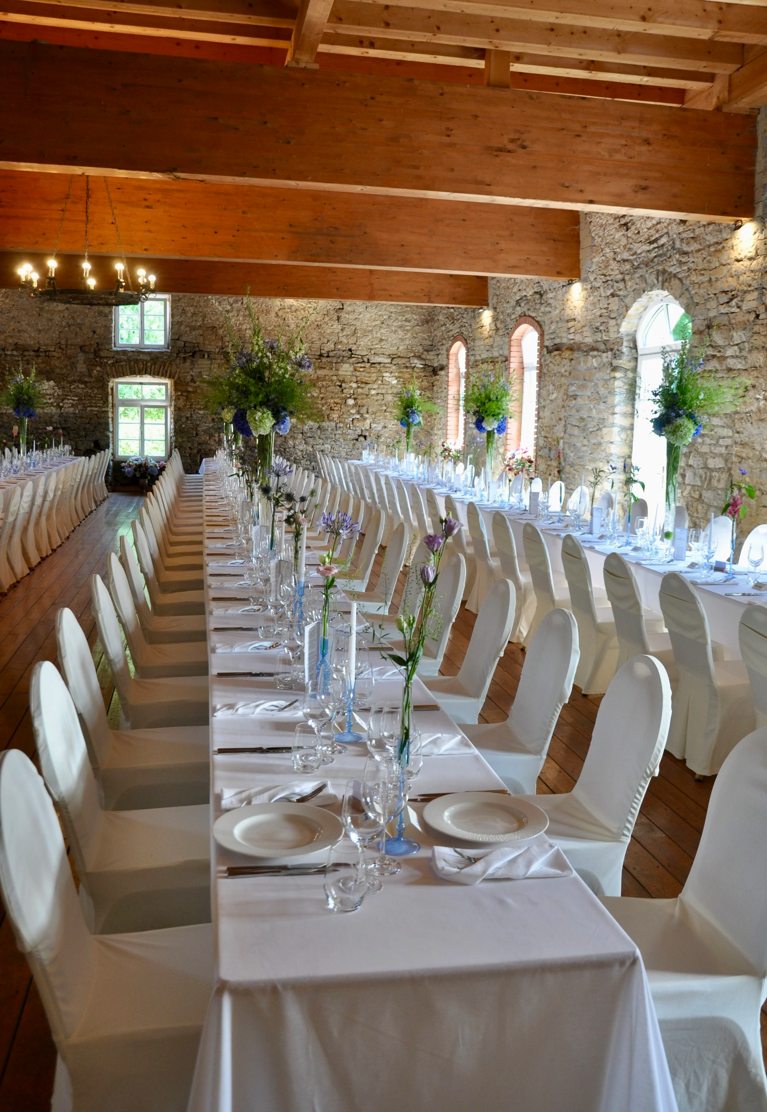 Festlich gedeckter Saal mit weißen Tischen, Blumenarrangements und Holzdecke in einer alten Steinfestung.