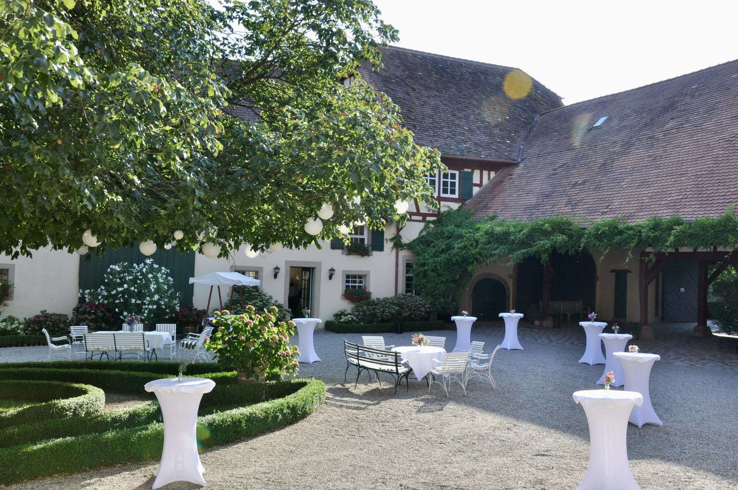 Menschen sammeln sich im Innenhof von Gut Schwarzerdhof und lassen rosa Herzballons in den Himmel steigen. Im Hintergrund sind traditionelle Fachwerkhäuser und eine große Kastanie zu sehen.