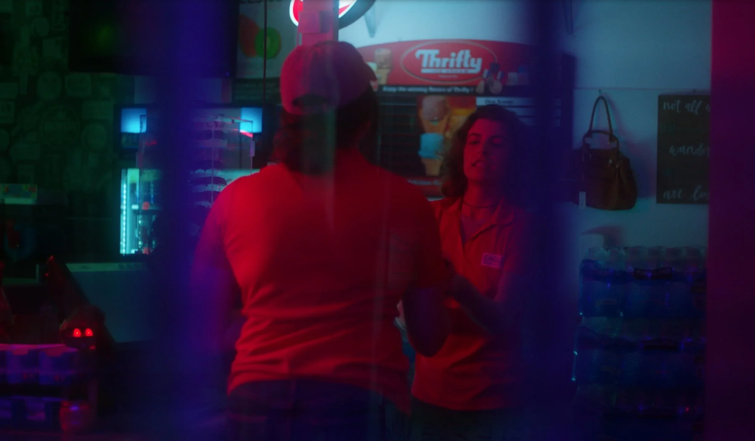 Blue and red themed still of the two coworkers in the gas station set of the film “Wolf in Lamb’s Skin.”