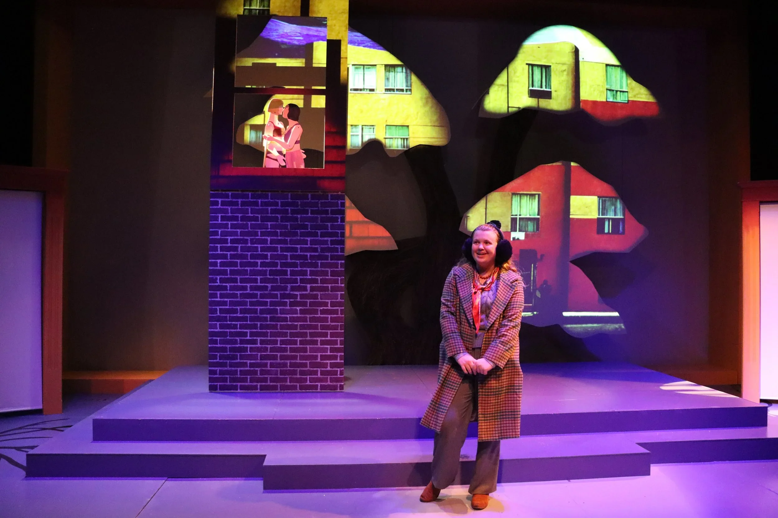 Claire, the youngest daughter, pictured underneath a window set piece with puppets operating inside, in front of a projected on tree on the set of the play “The Long Christmas Ride Home” by Paula Vogel