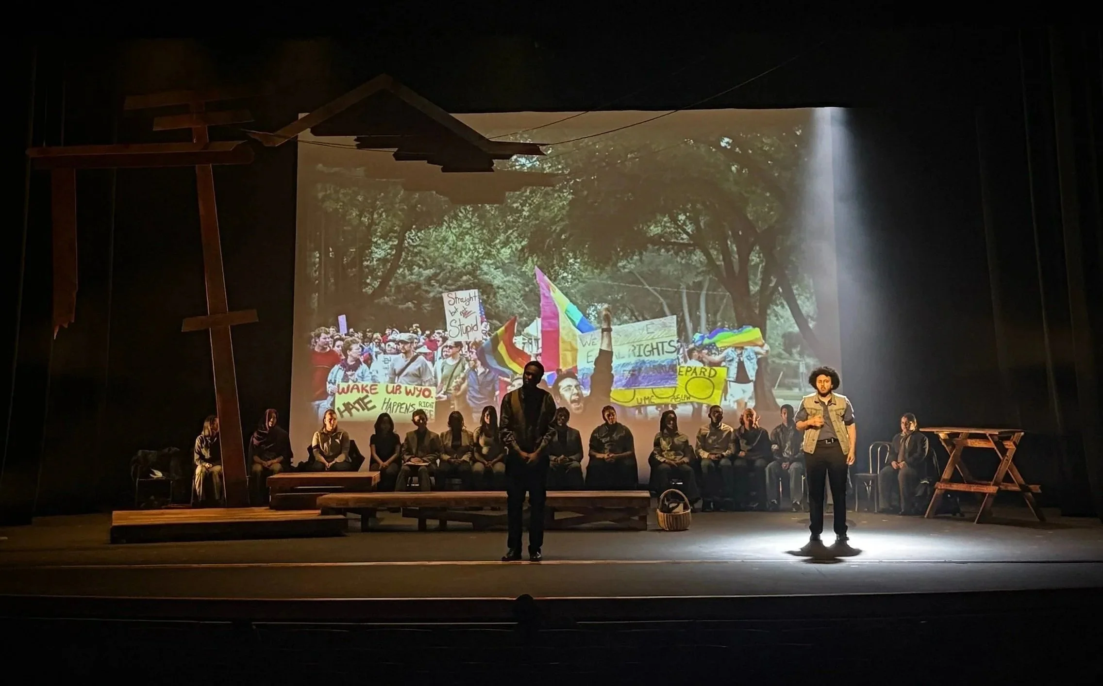 Spotlit actor in front of the pride parade projection design cue for the play “The Laramie Project” by Moises Kaufman and the Tectonic Theater Project