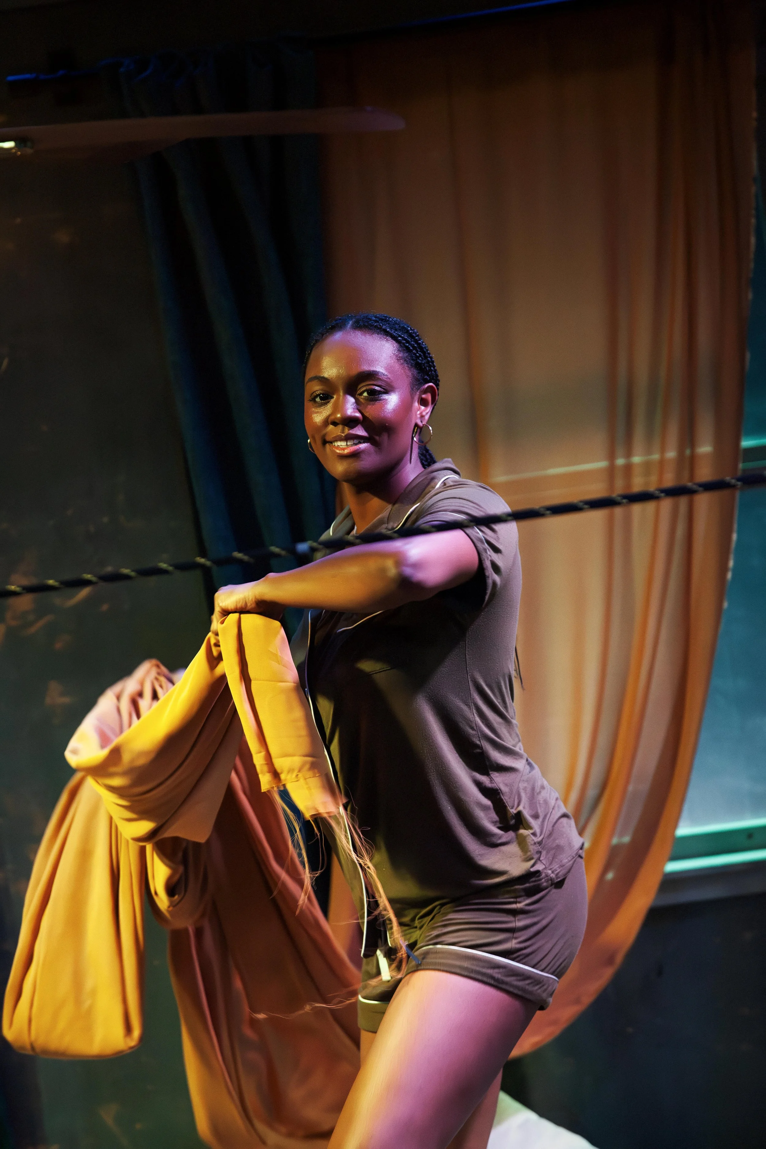 Mina throwing golden colorful fabric over a length of rope to build a fort during the play “Furlough’s Paradise” by A.K. Payne