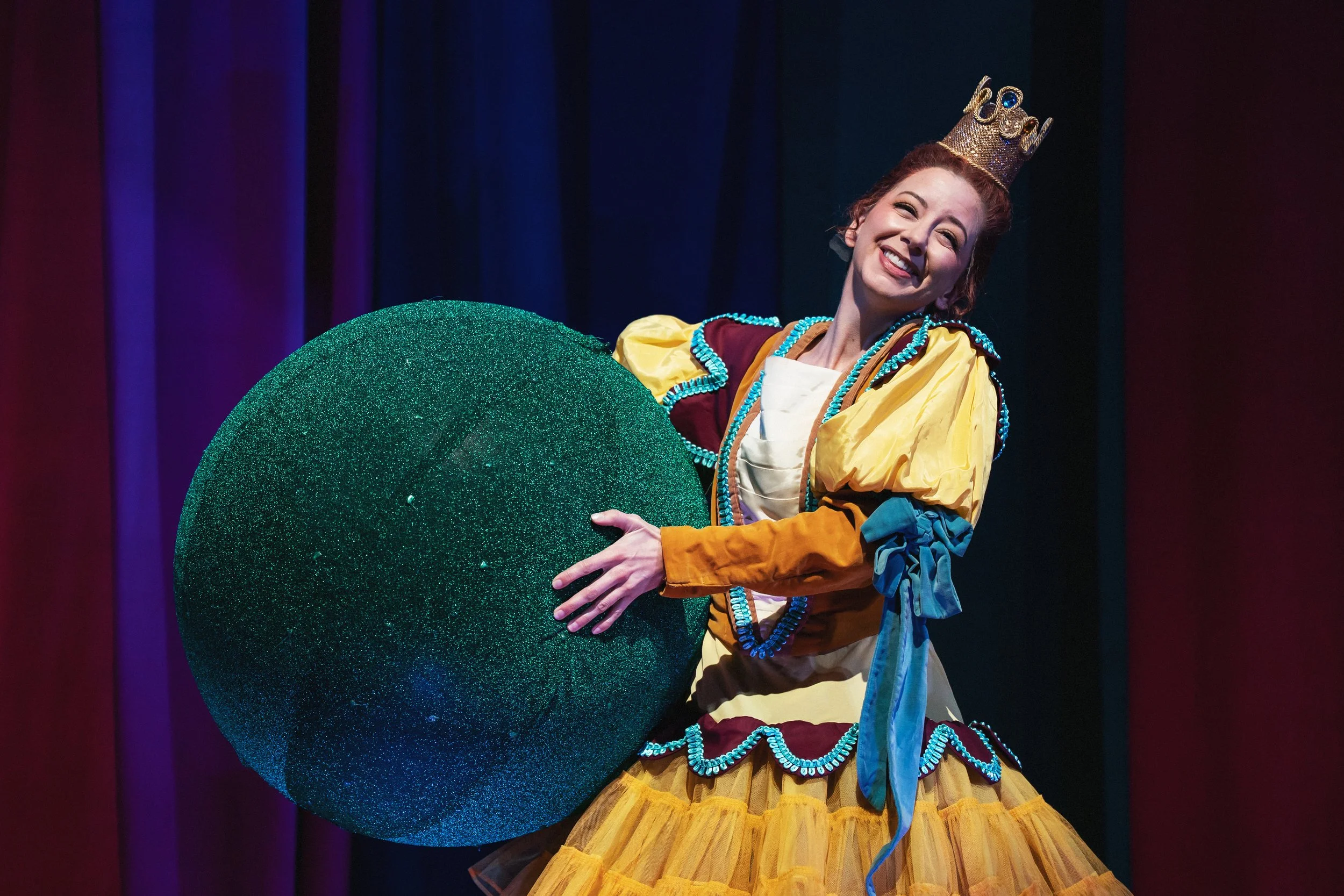 A dancer holding a gigantic sparkly pea in the opening scene of the opera “Once Upon a Mattress”
