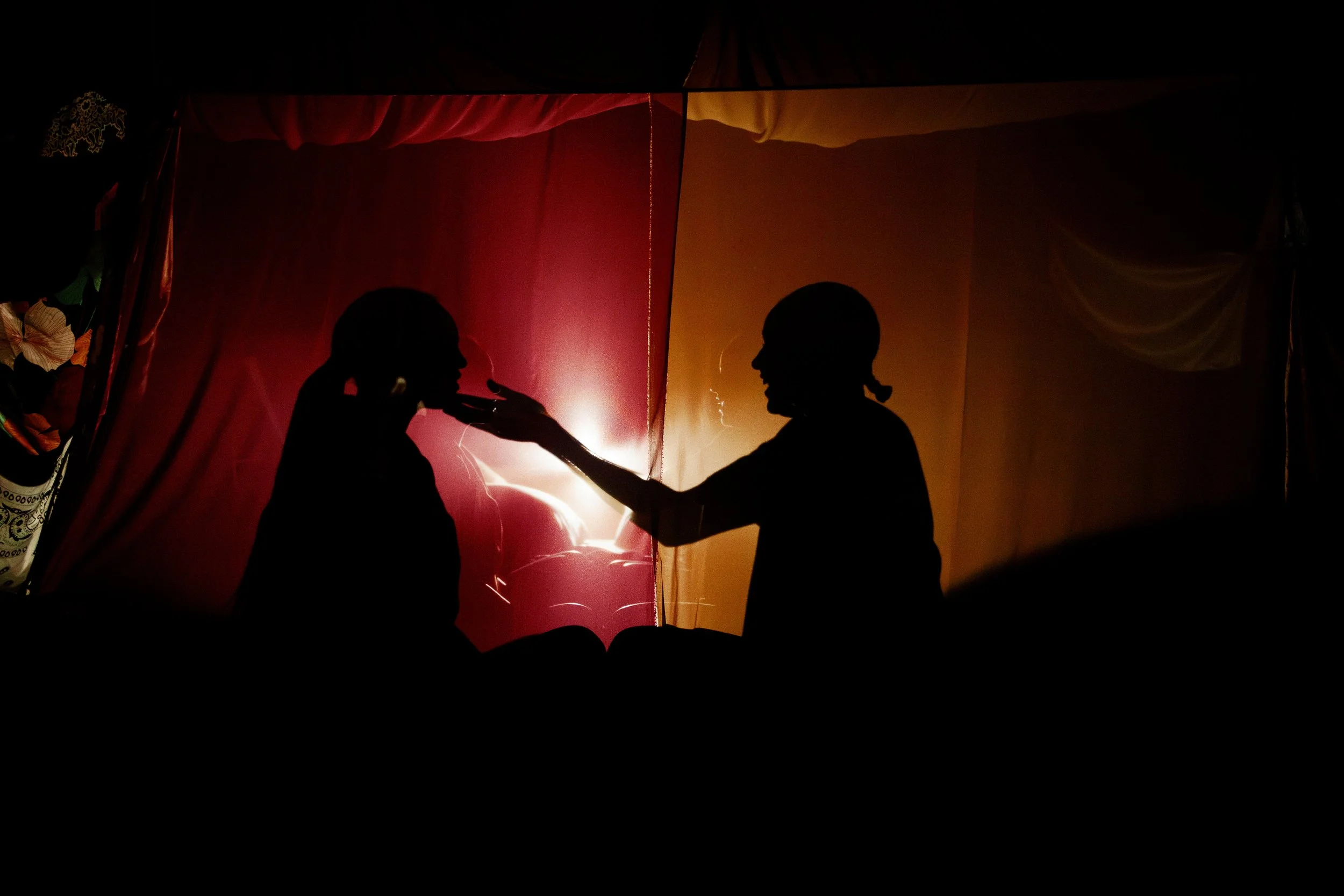 Silhouetted actresses on red and gold fabric, sitting inside the fort they built onstage, during the play “Furlough’s Paradise” by A.K. Payne