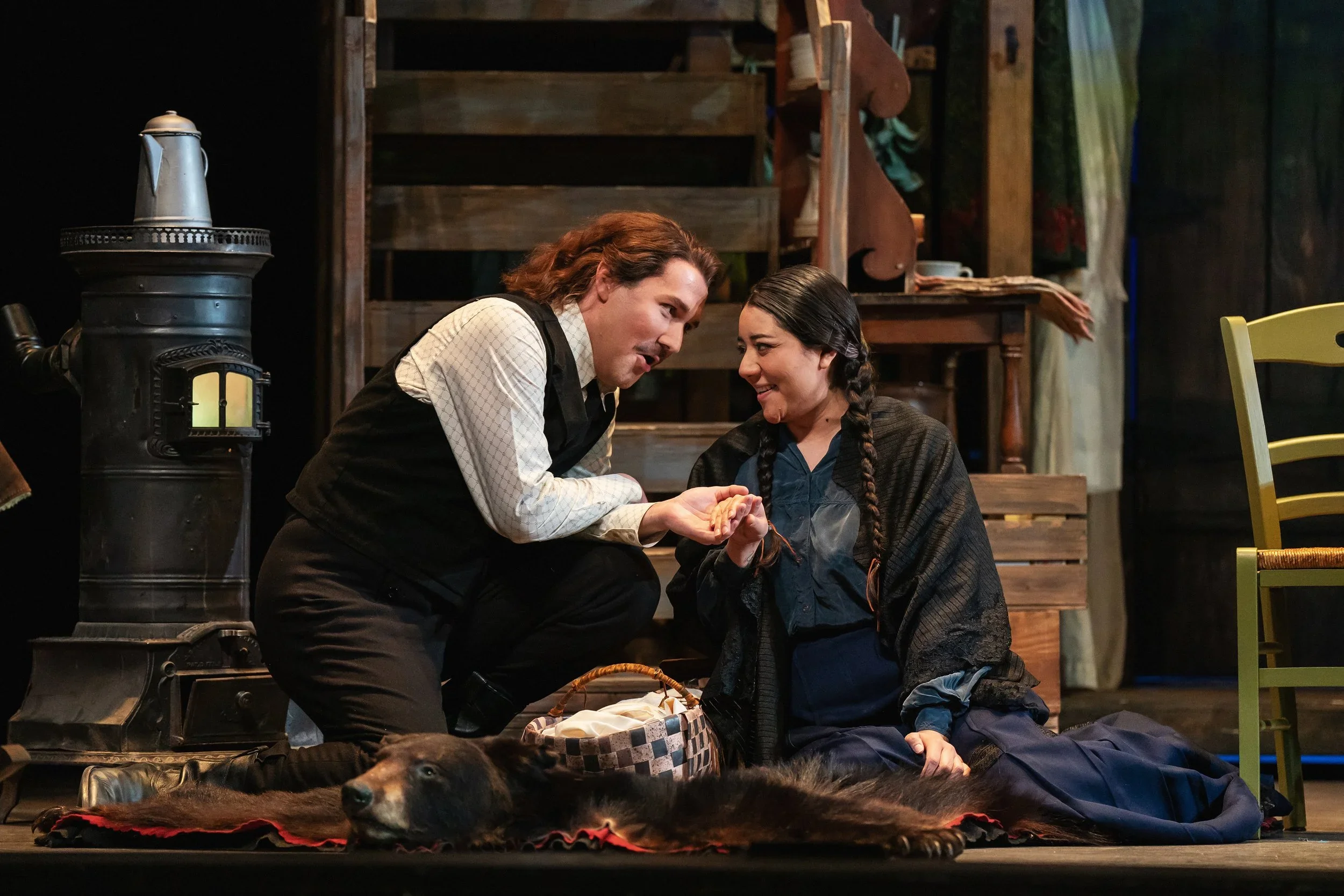 Close-up of characters on a bear rug with a paper woven baby basket in the opera “La Fanciulla del West”