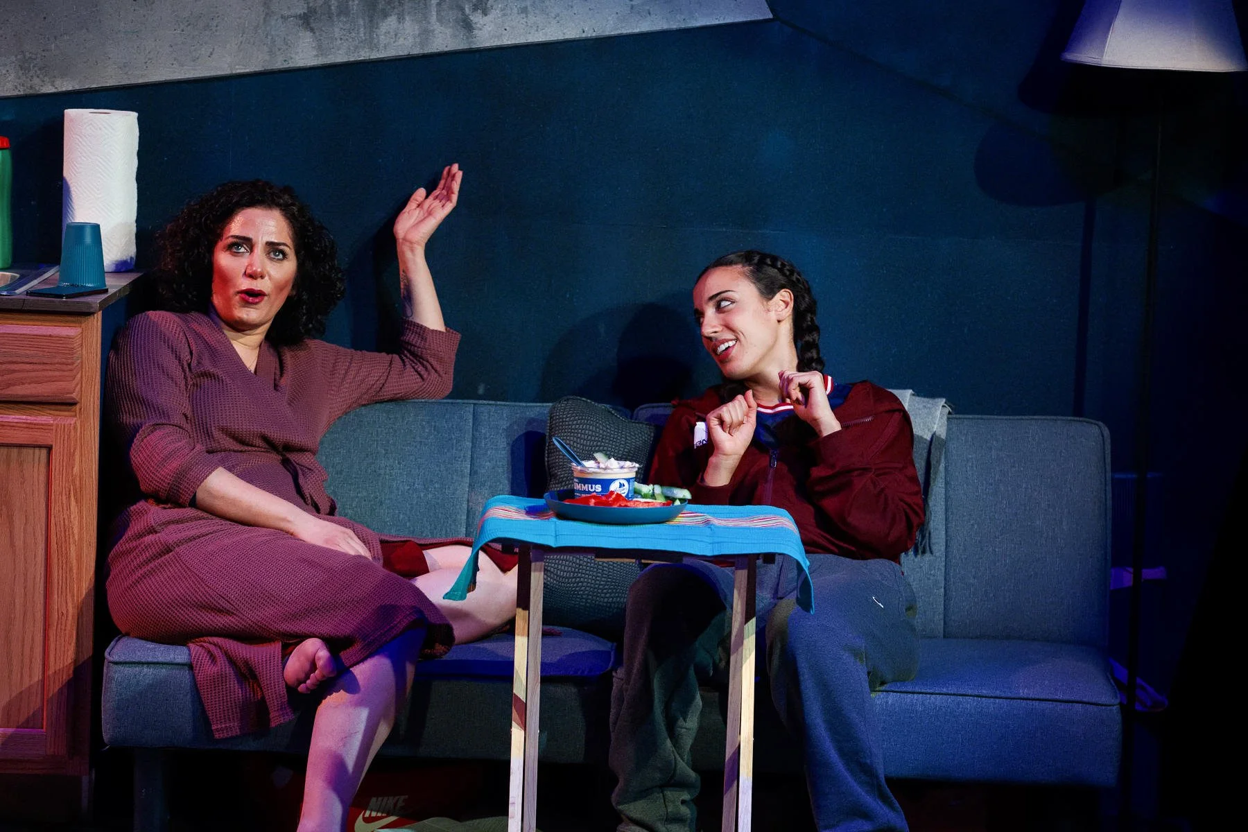 Mom and daughter eating a meal on a couch in the play “American Fast” by Kareem Fahmy