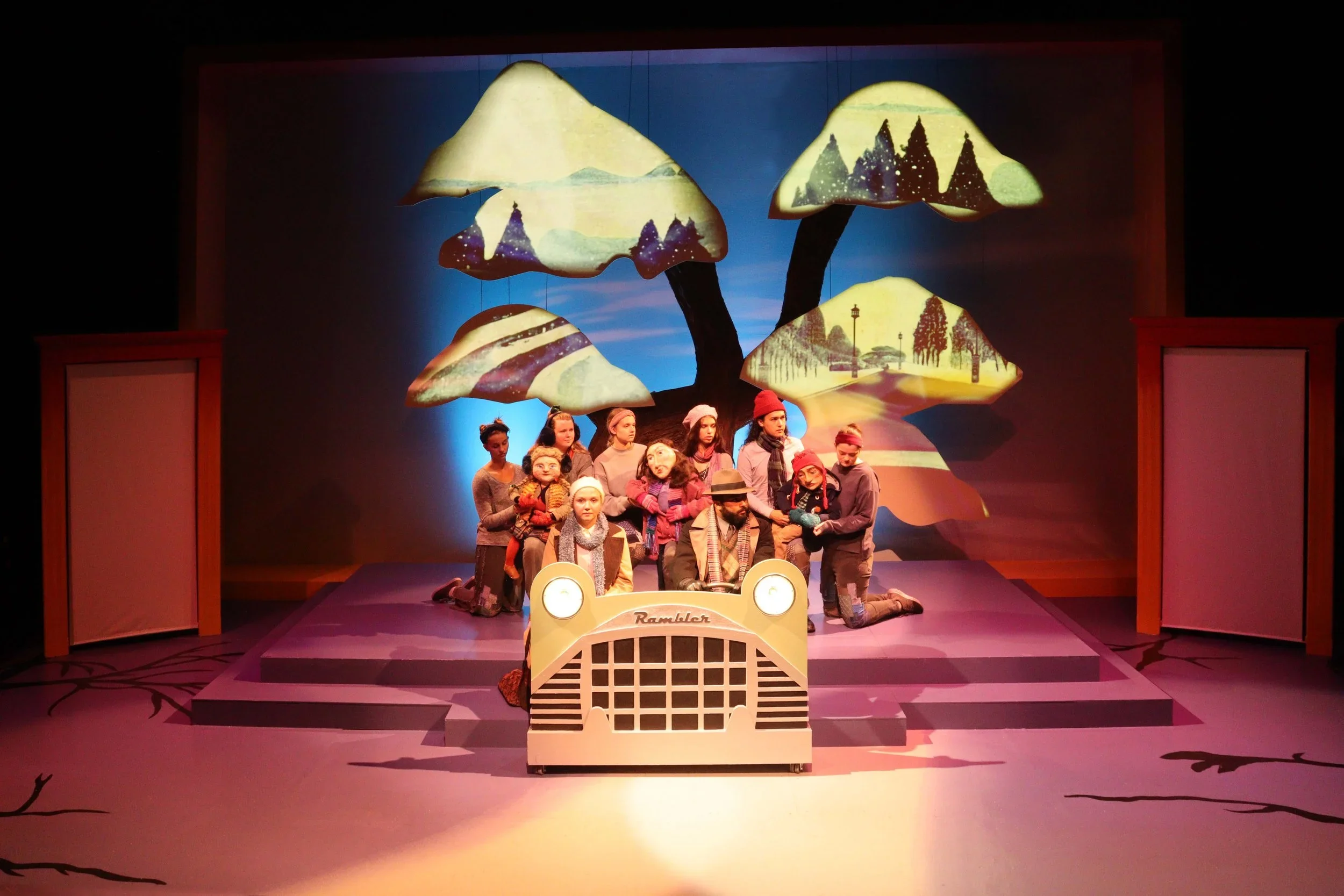 Wide shot of the set, car set piece, and projections on the tree of the play “The Long Christmas Ride Home” by Paula Vogel