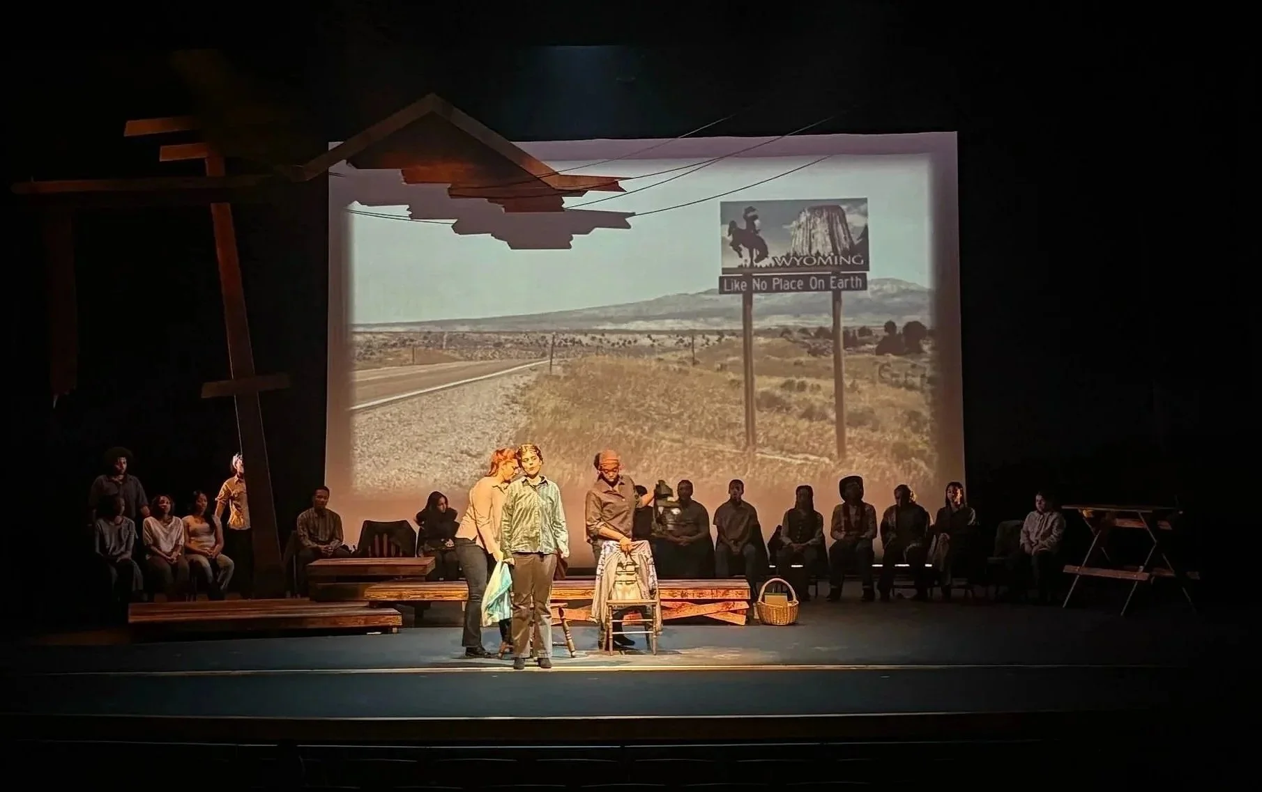 Actors backed with projection design of the entrance to Laramie Wyoming for the play “The Laramie Project” by Moises Kaufman and the Tectonic Theater Project