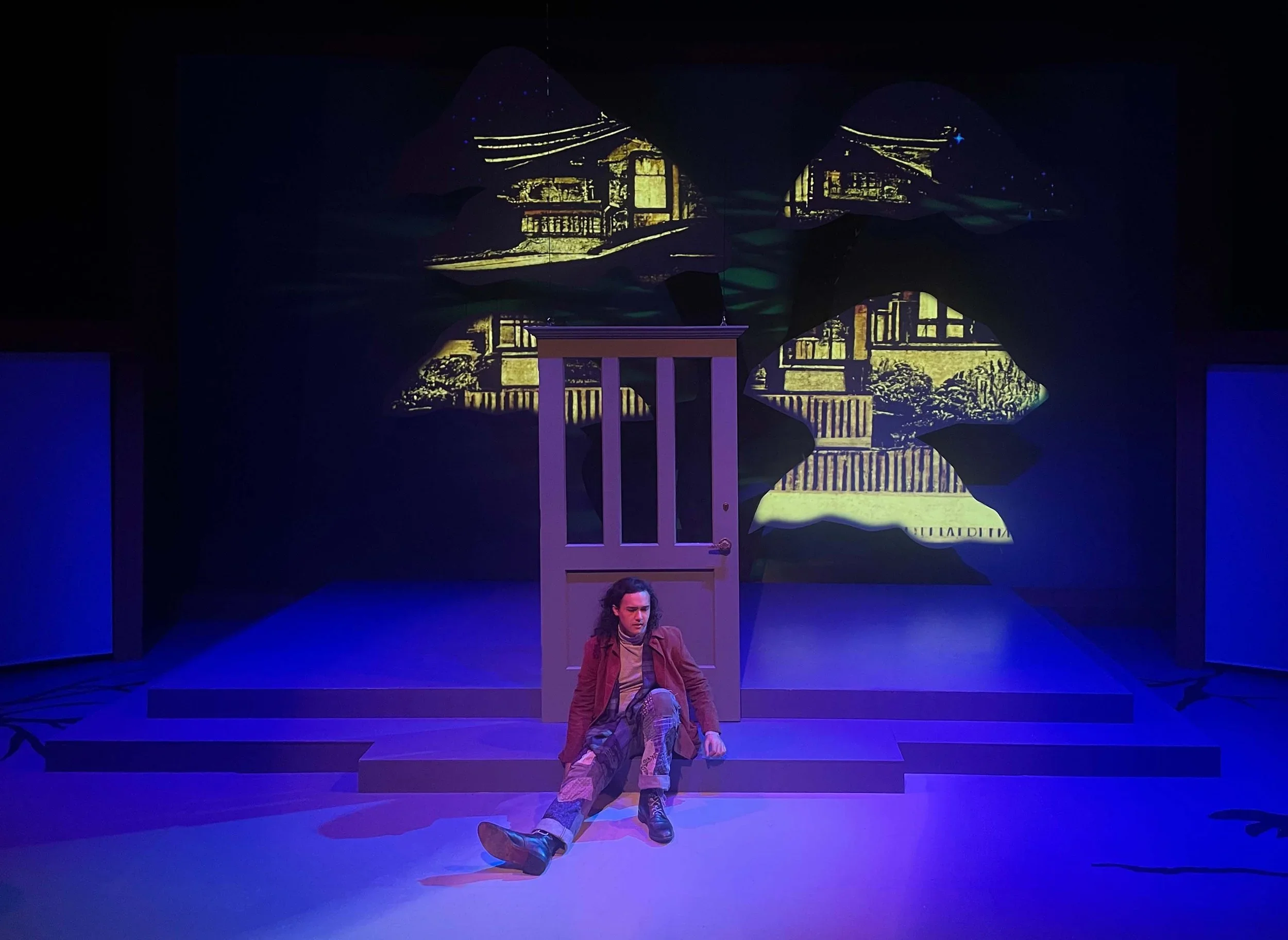 Shot of Stephen sitting in front of a flown in door on the scenic design of the play “The Long Christmas Ride Home” by Paula Vogel