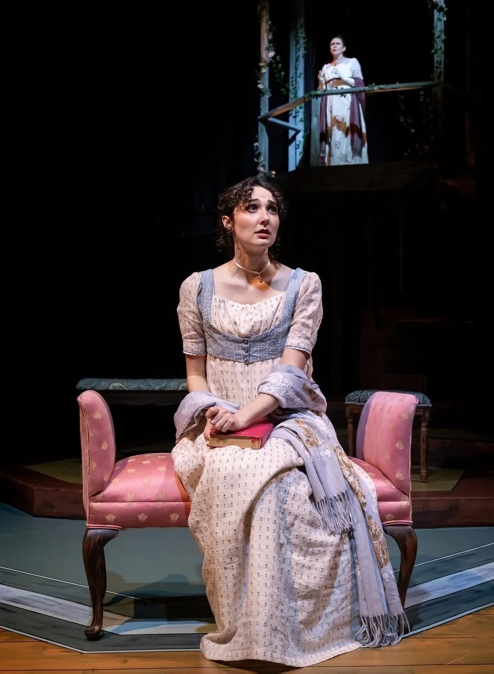 Anne sitting on a chaise with a bright red book in the play “Persuasion” by Jane Austen, adapted by Sarah Rose Kearns